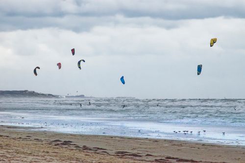 Free Vibrant kitesurfers ride the waves on a windy, cloudy beach day. Stock Photo