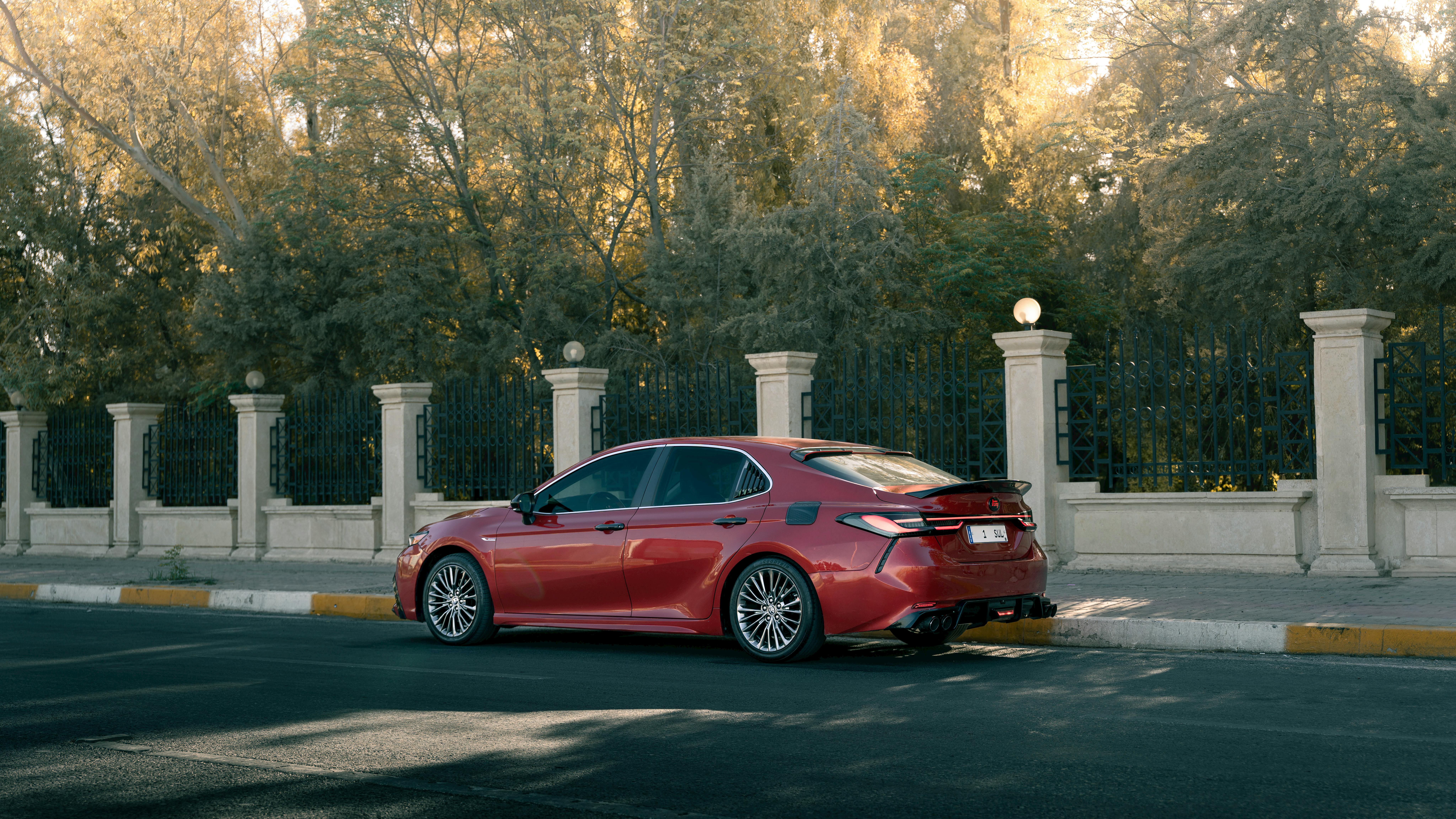 Free Stylish red sedan car parked beside ornate fence in sunlight, showcasing modern design. Stock Photo