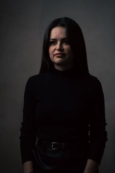 A dramatic portrait of a woman in a dark, moody setting wearing a black turtleneck.