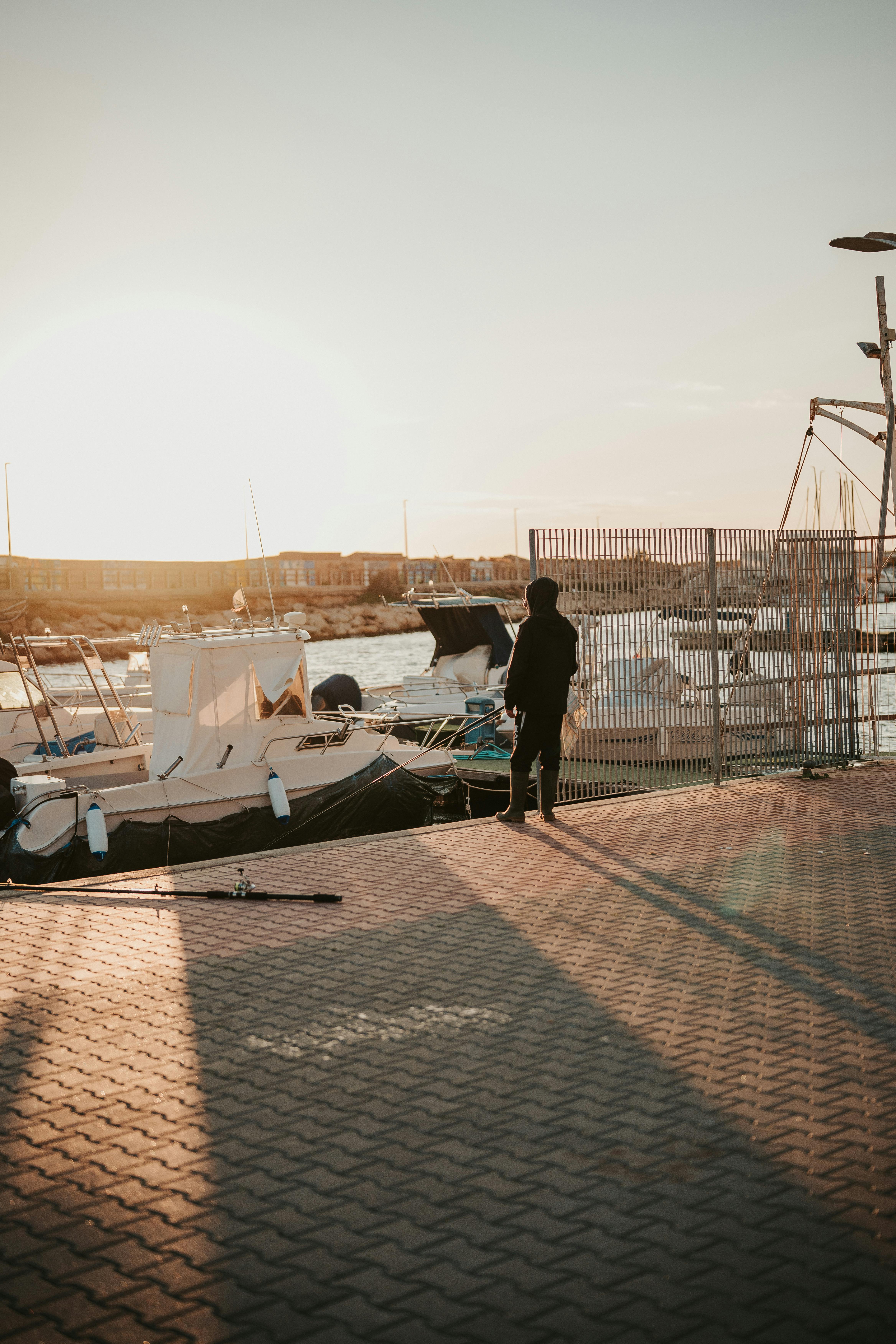 Gratuit Silueta unei persoane care stă lângă bărci la un port de agrement în timpul apusului, creând o scenă de coastă senină. Fotografie de stoc