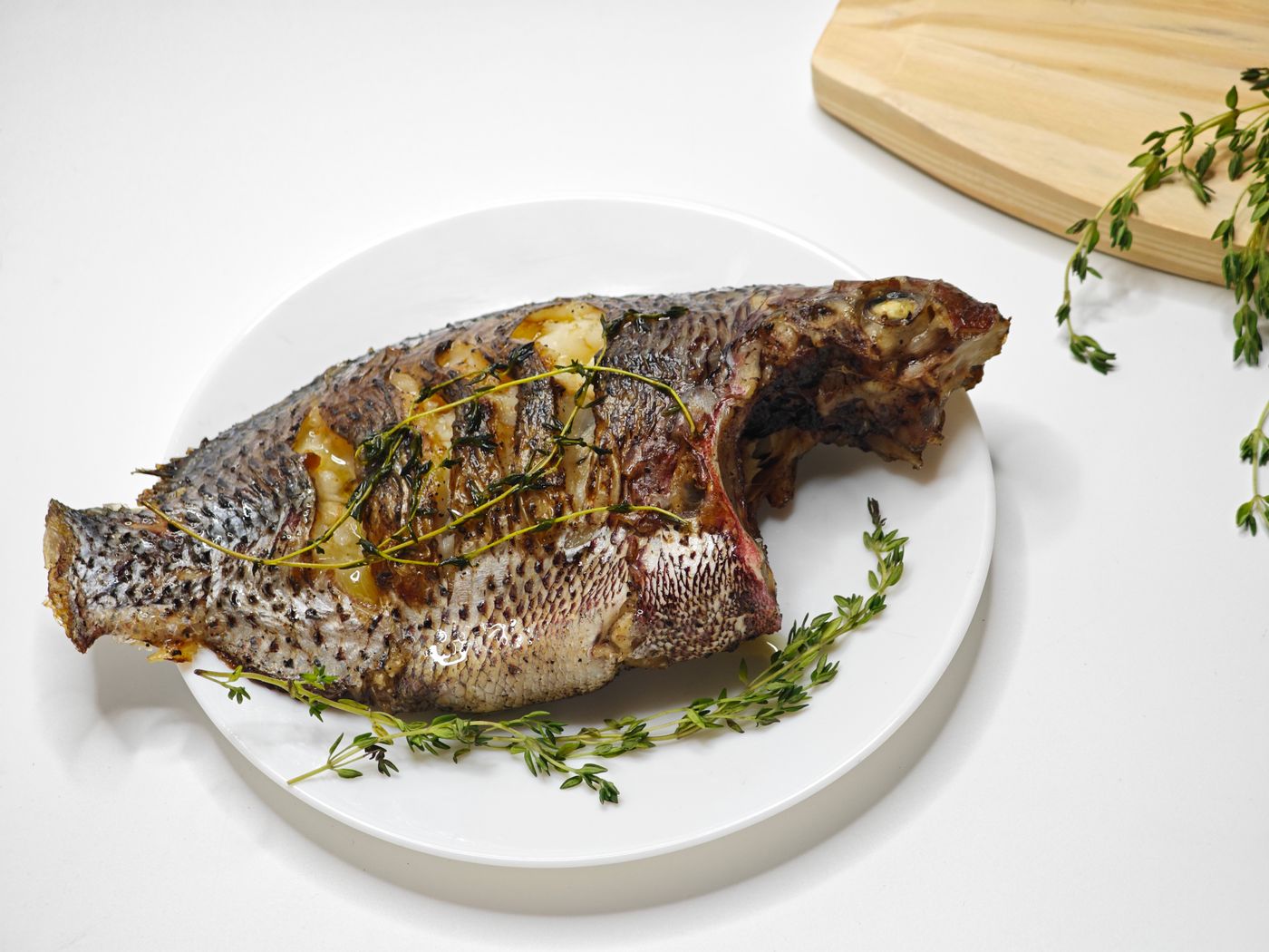 Grilled whole fish garnished with fresh thyme on a white platter.