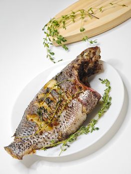 Delicious grilled whole fish seasoned with fresh herbs on a white platter.