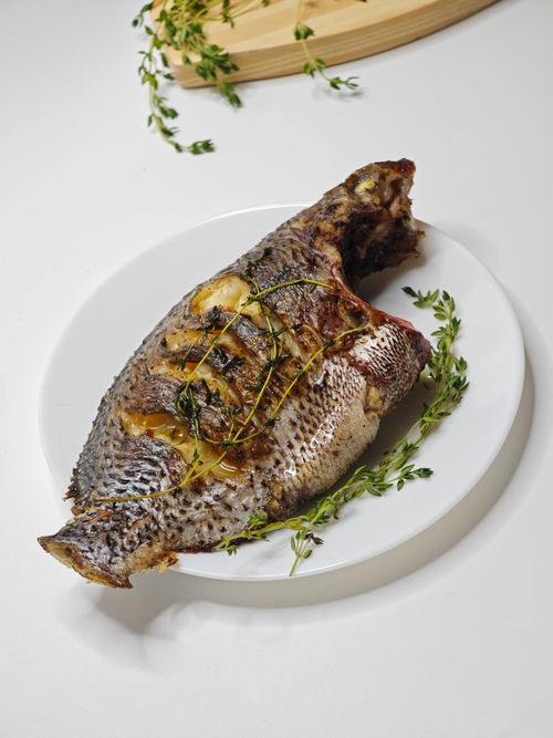 Free Delicious grilled whole fish garnished with fresh herbs on a white plate. Perfect for seafood lovers. Stock Photo