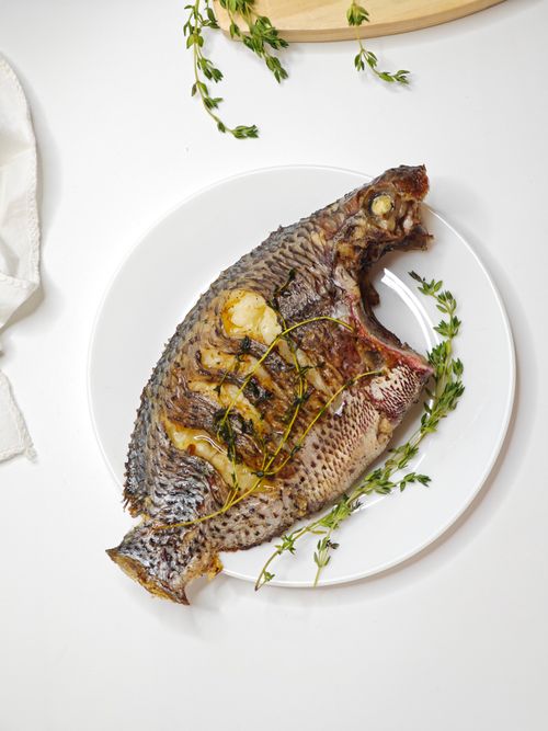 Free Delicious grilled tilapia garnished with fresh herbs on a white plate, perfect for culinary presentations. Stock Photo
