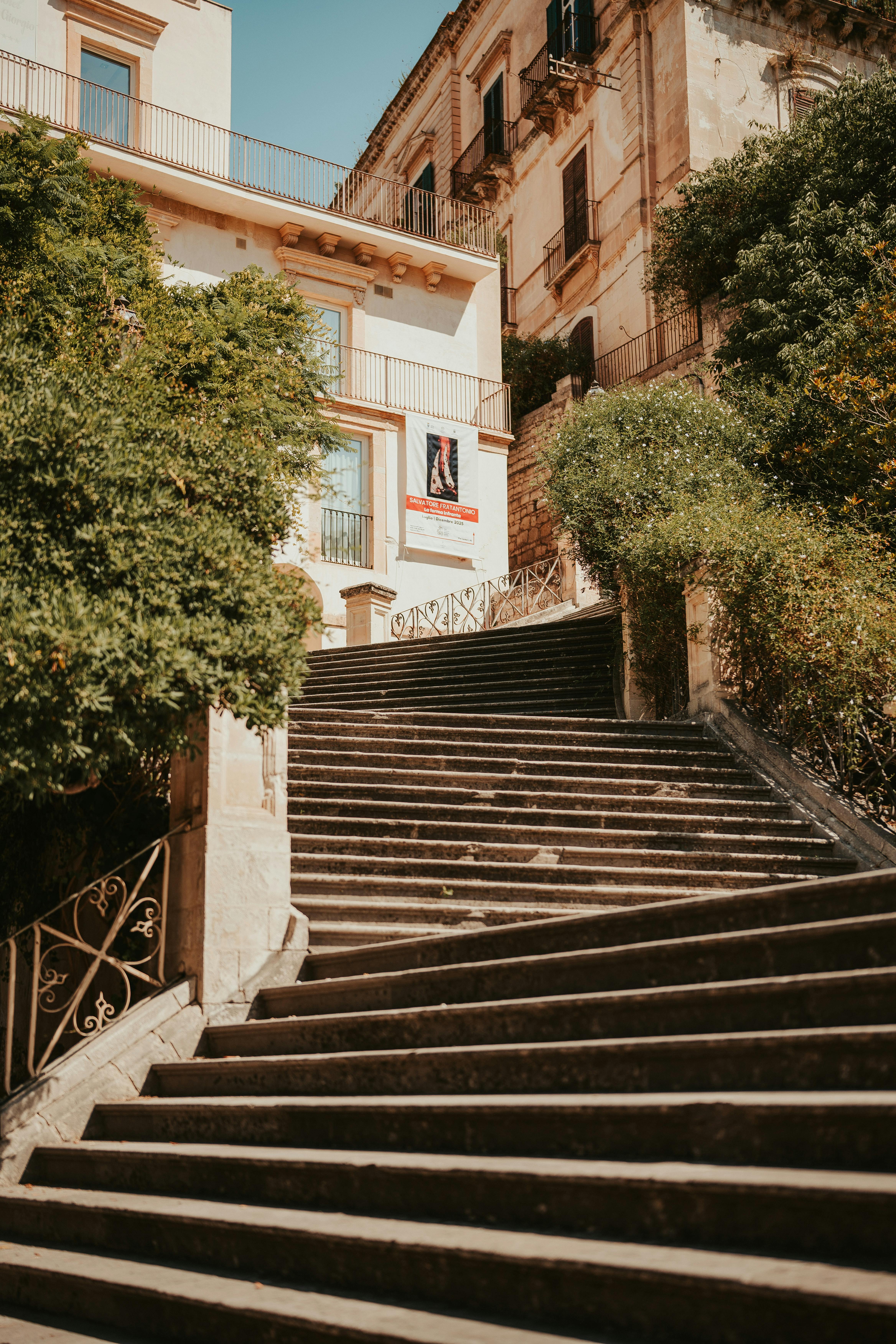 Free Charming stone staircase in Modica, Sicily, Italy surrounded by lush greenery under a bright blue sky. Stock Photo