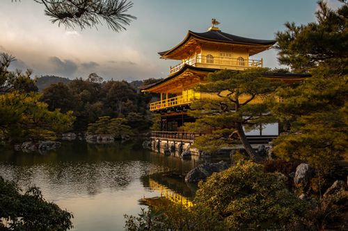 Free Stunning view of Kinkaku-ji reflected in a serene pond under the warm sunset light. Stock Photo