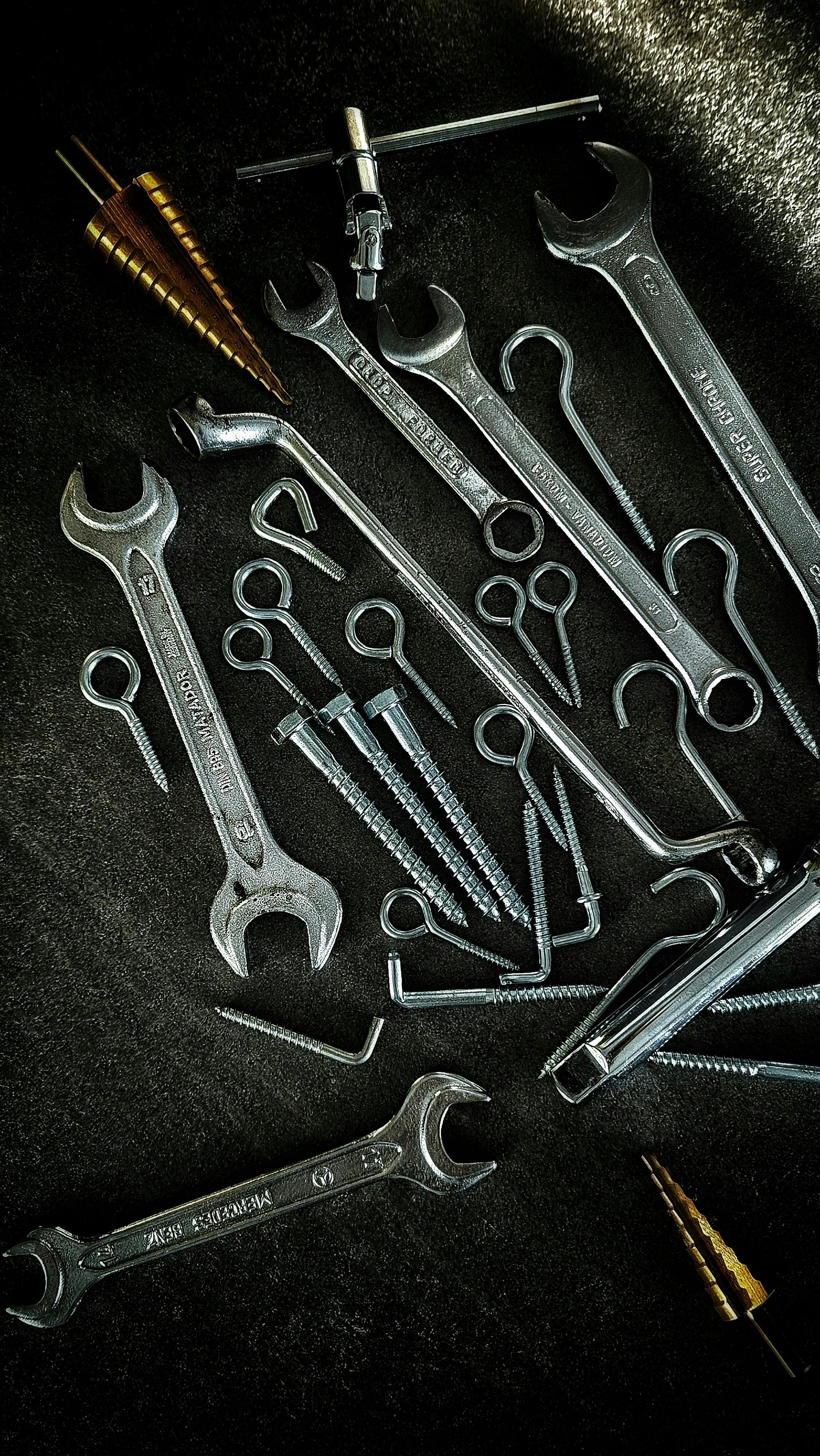 Free A collection of metal wrenches, screws, and drill bits arranged artistically on a dark background. Stock Photo