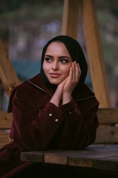 Smiling woman in a hijab sitting outdoors on a wooden bench.
