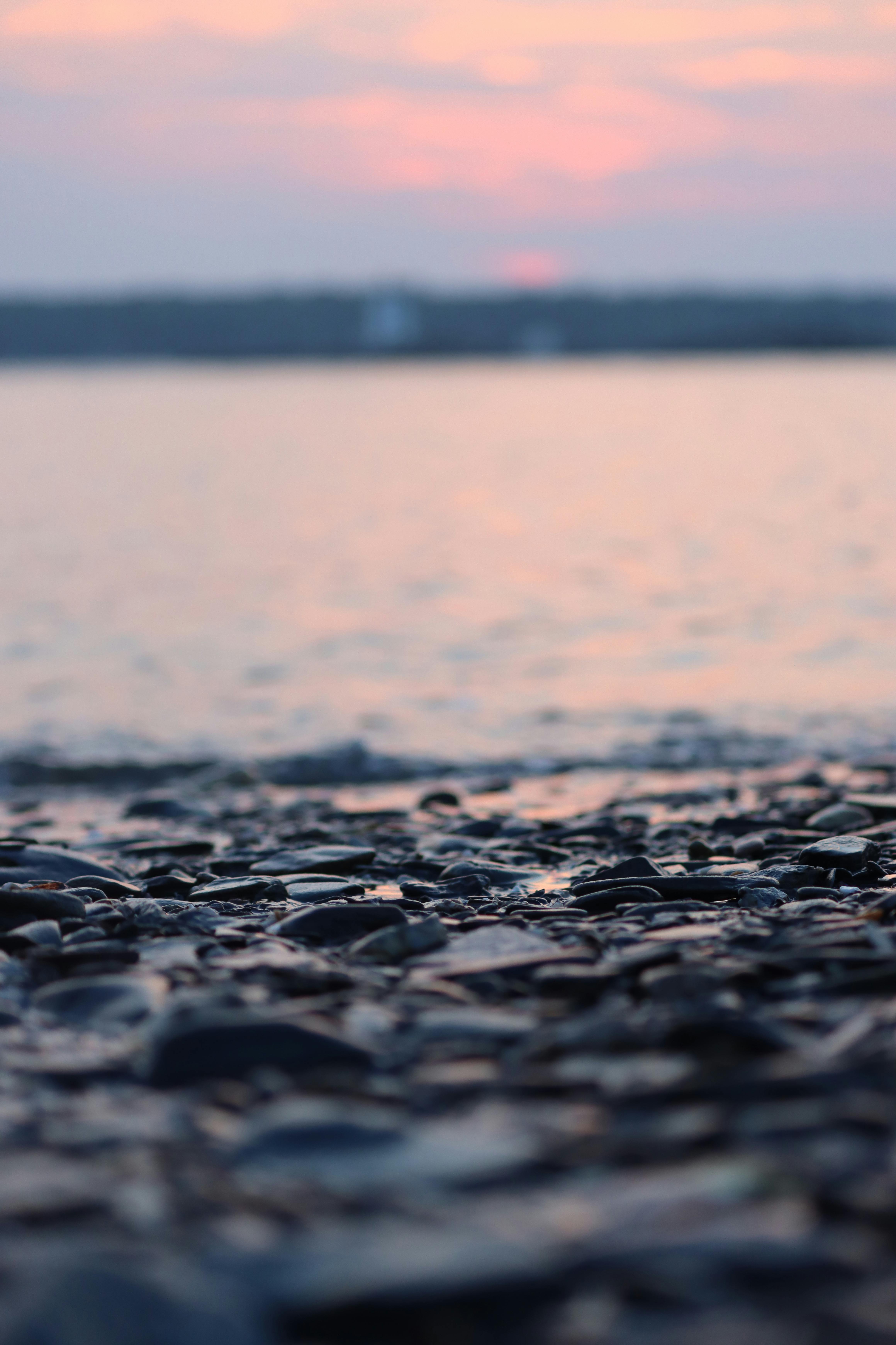無料 水面に沈む柔らかな夕日と小石の海岸の静かな景色。 写真素材