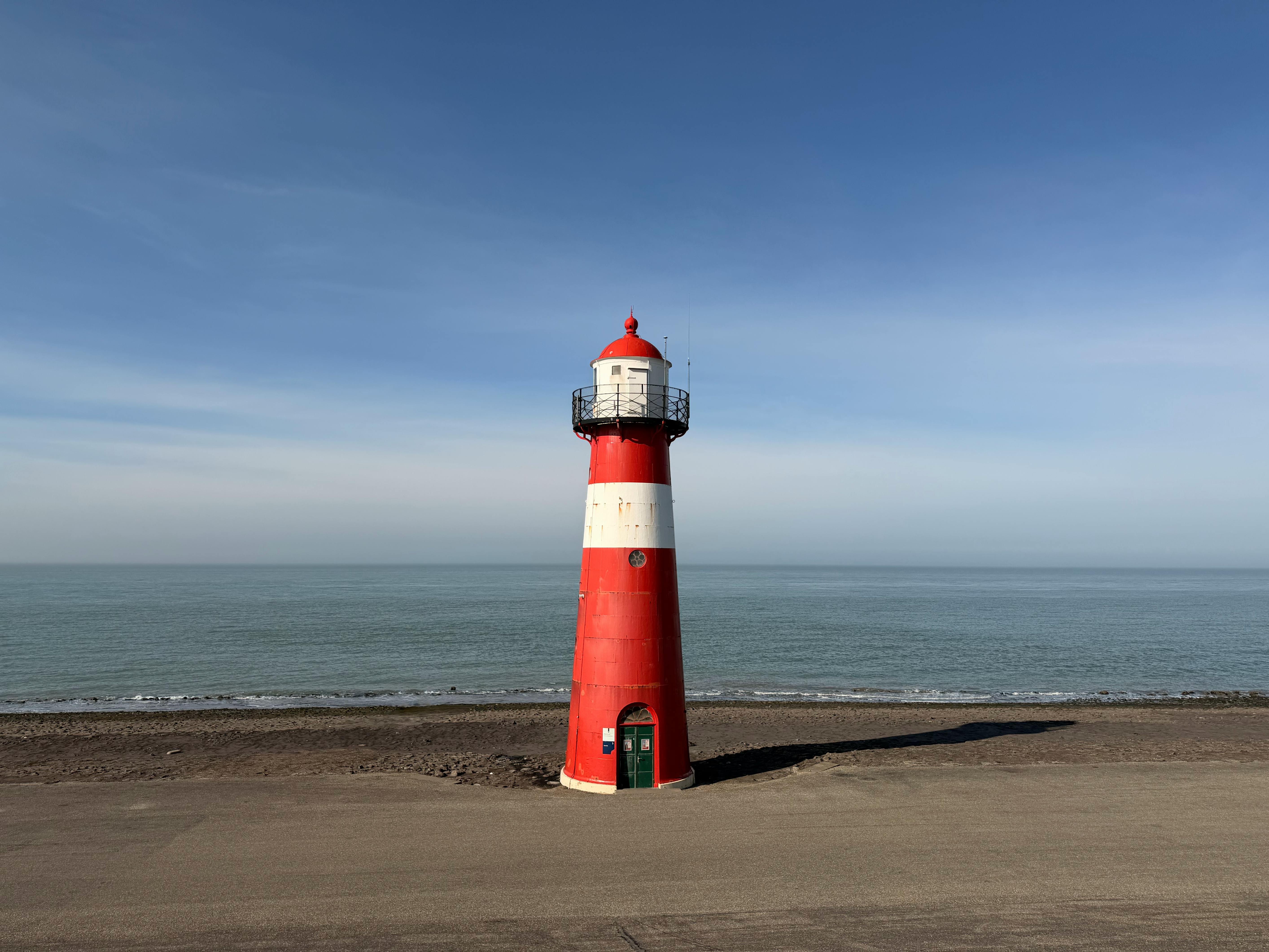 無料 澄んだ空の下、静かな海岸沿いに立つ赤と白の灯台。 写真素材