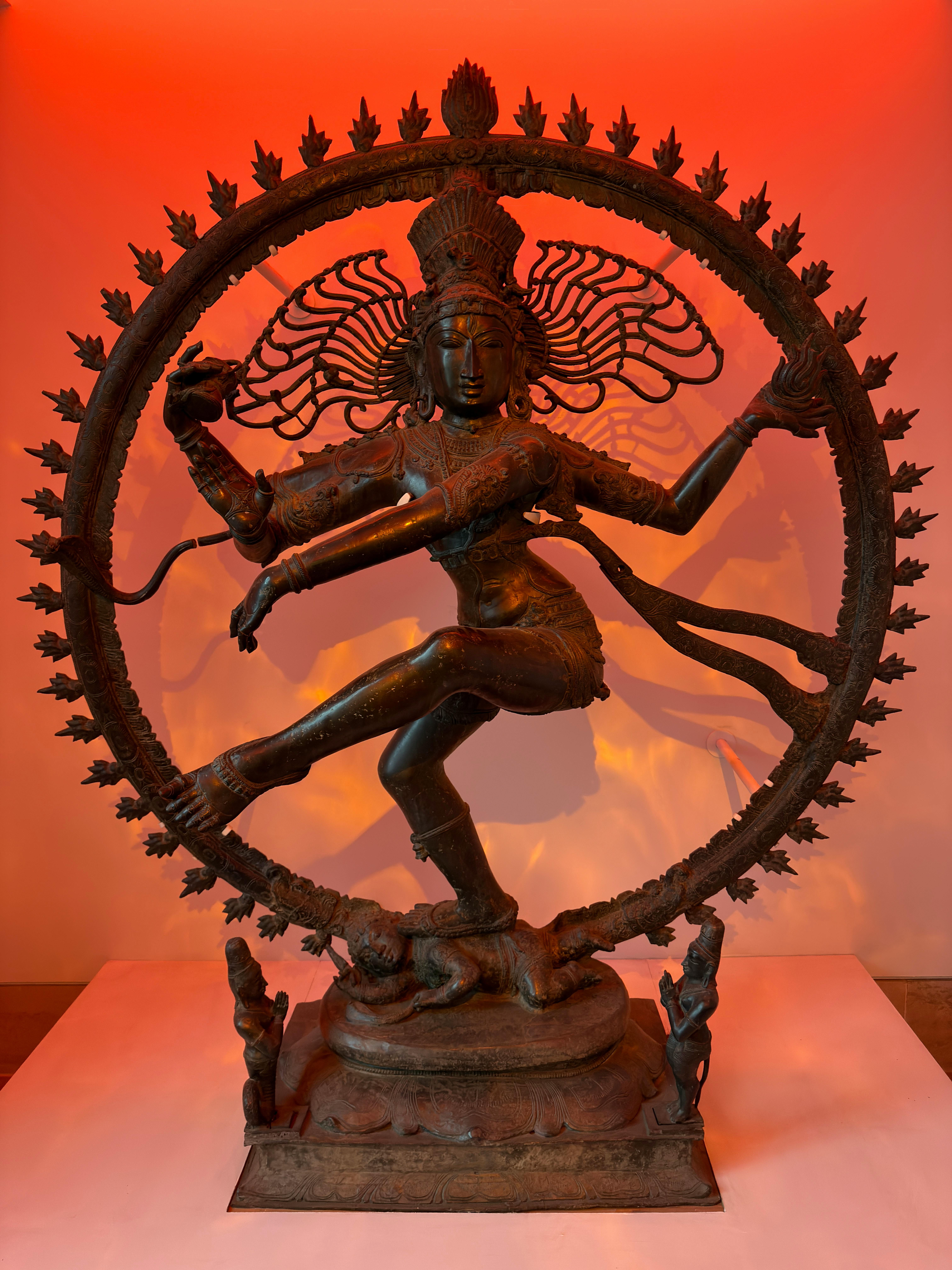 無料 鮮やかなオレンジ色の照明を背景にしたナタラジャの精巧なブロンズ彫刻が、ダイナミックな動きを捉えています。 写真素材