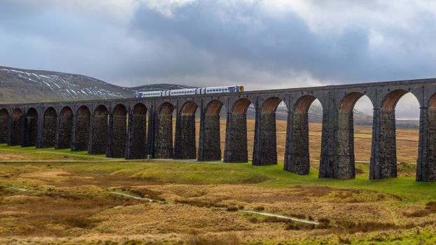Train crossing the historic Ribblehead Viaduct in the scenic Yorkshire Dales, UK.