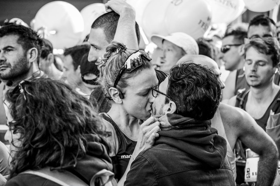 A couple sharing a kiss at a crowded marathon event, capturing a moment of affection.