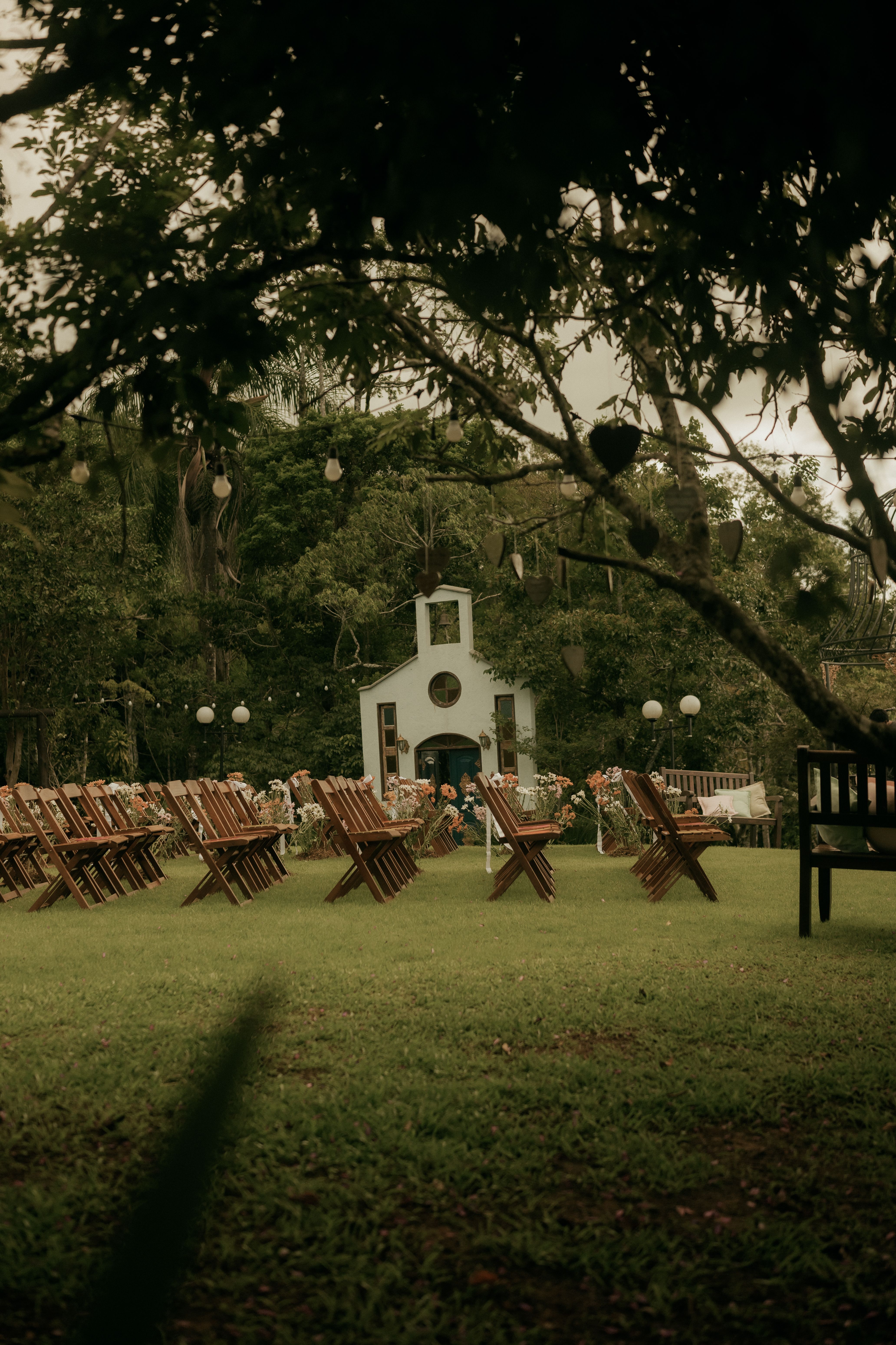 A serene outdoor wedding venue with rustic wooden chairs and a quaint chapel, perfect for nature lovers.