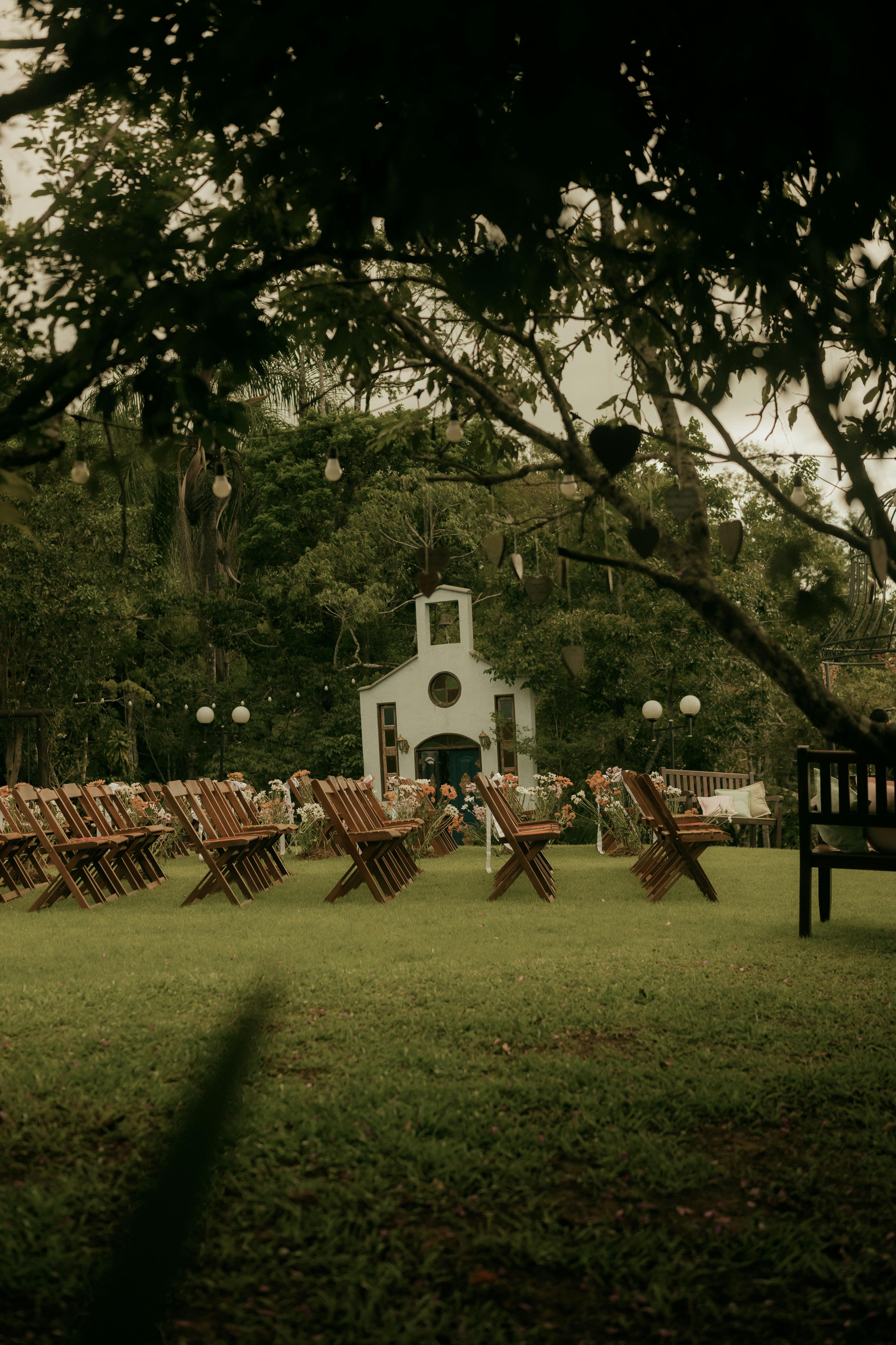 Gratis Et roligt udendørs bryllupssted med rustikke træstole og et hyggeligt kapel, perfekt for naturelskere. Lagerfoto