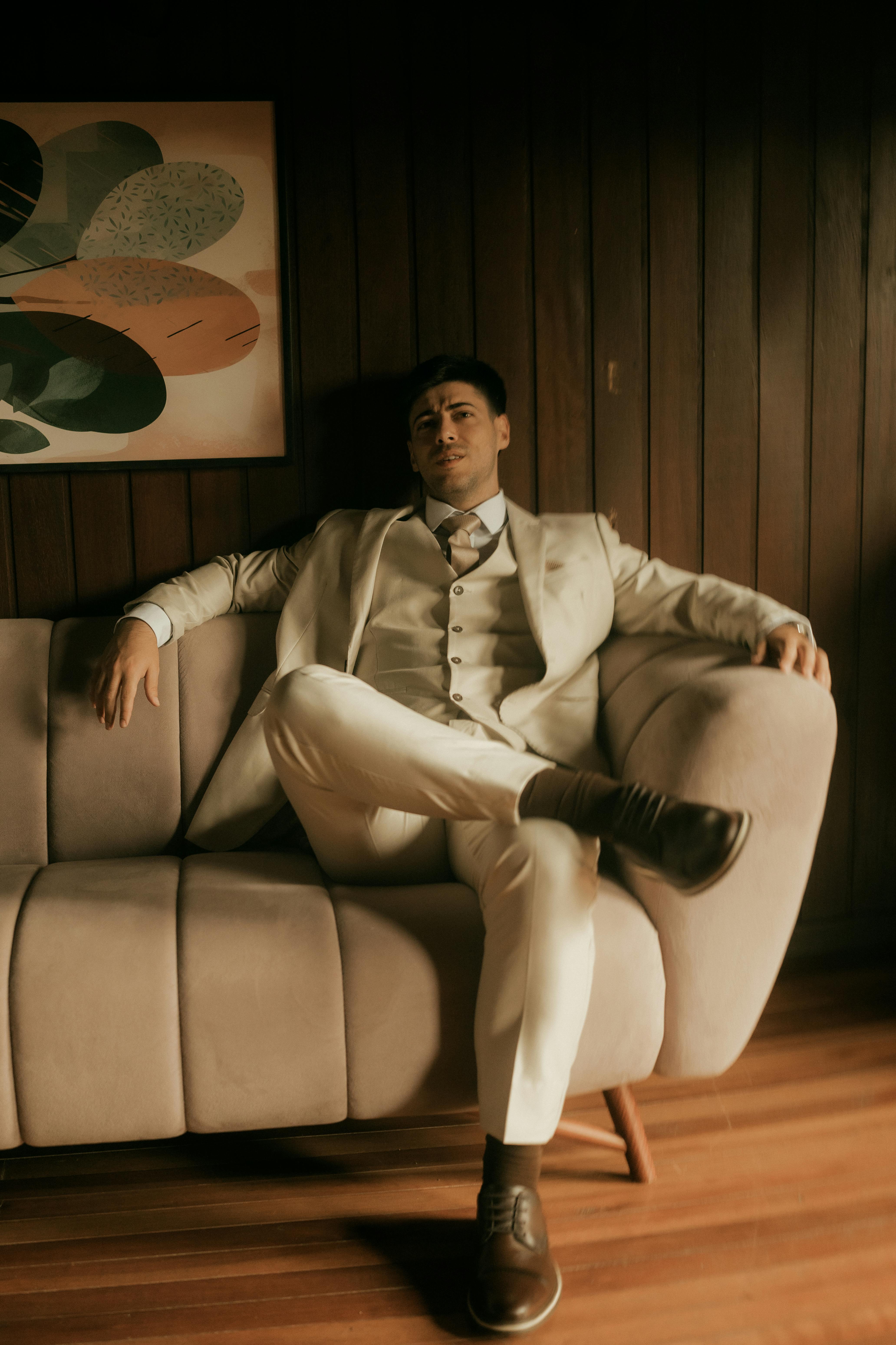 бесплатная Уверенный в себе мужчина в деловом костюме отдыхает на современном диване в стильной комнате. Стоковое фото