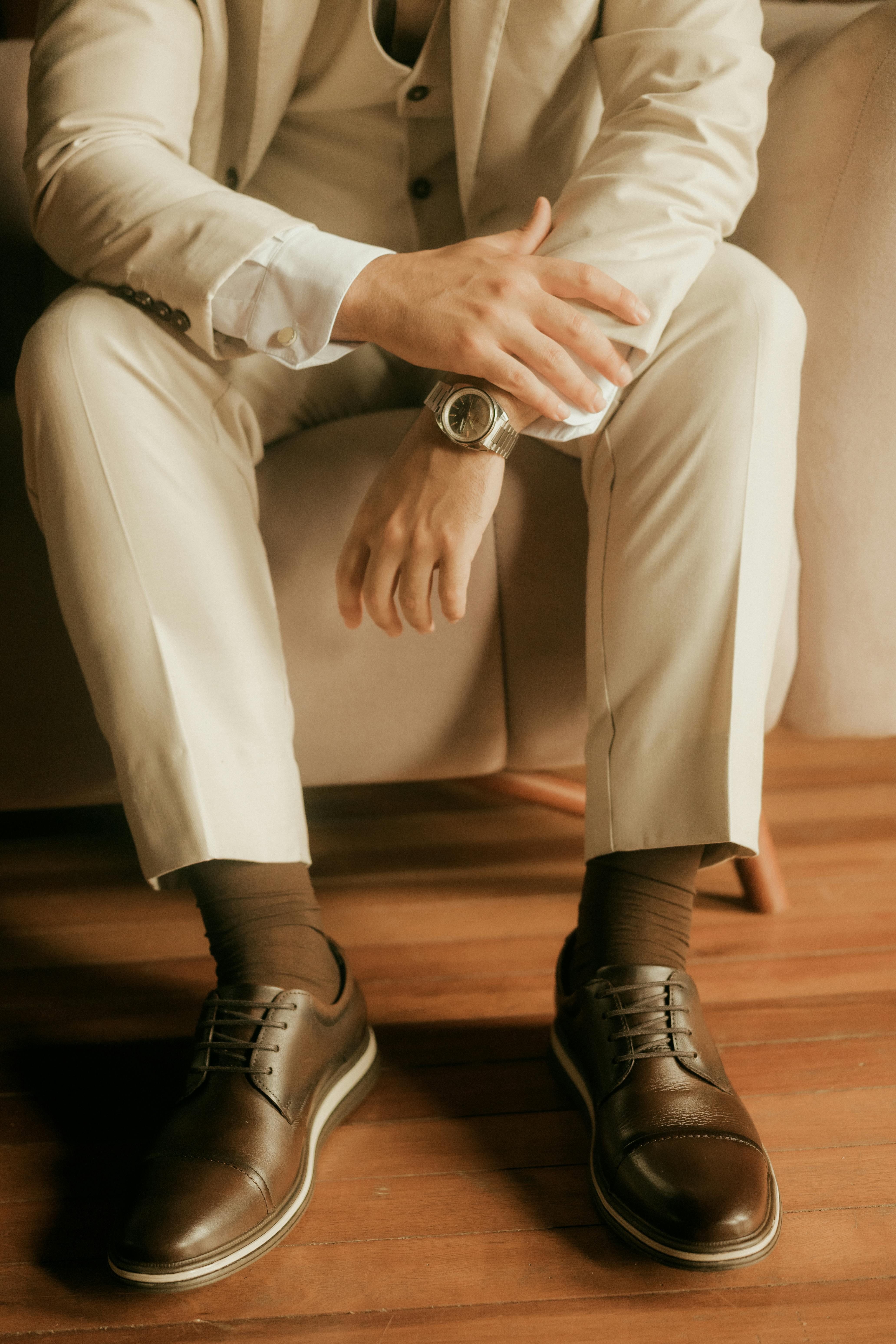 Kostenlos Ein eleganter Mann im beigen Anzug sitzt lässig da, dazu trägt er stilvolle braune Lederschuhe. Stock-Foto