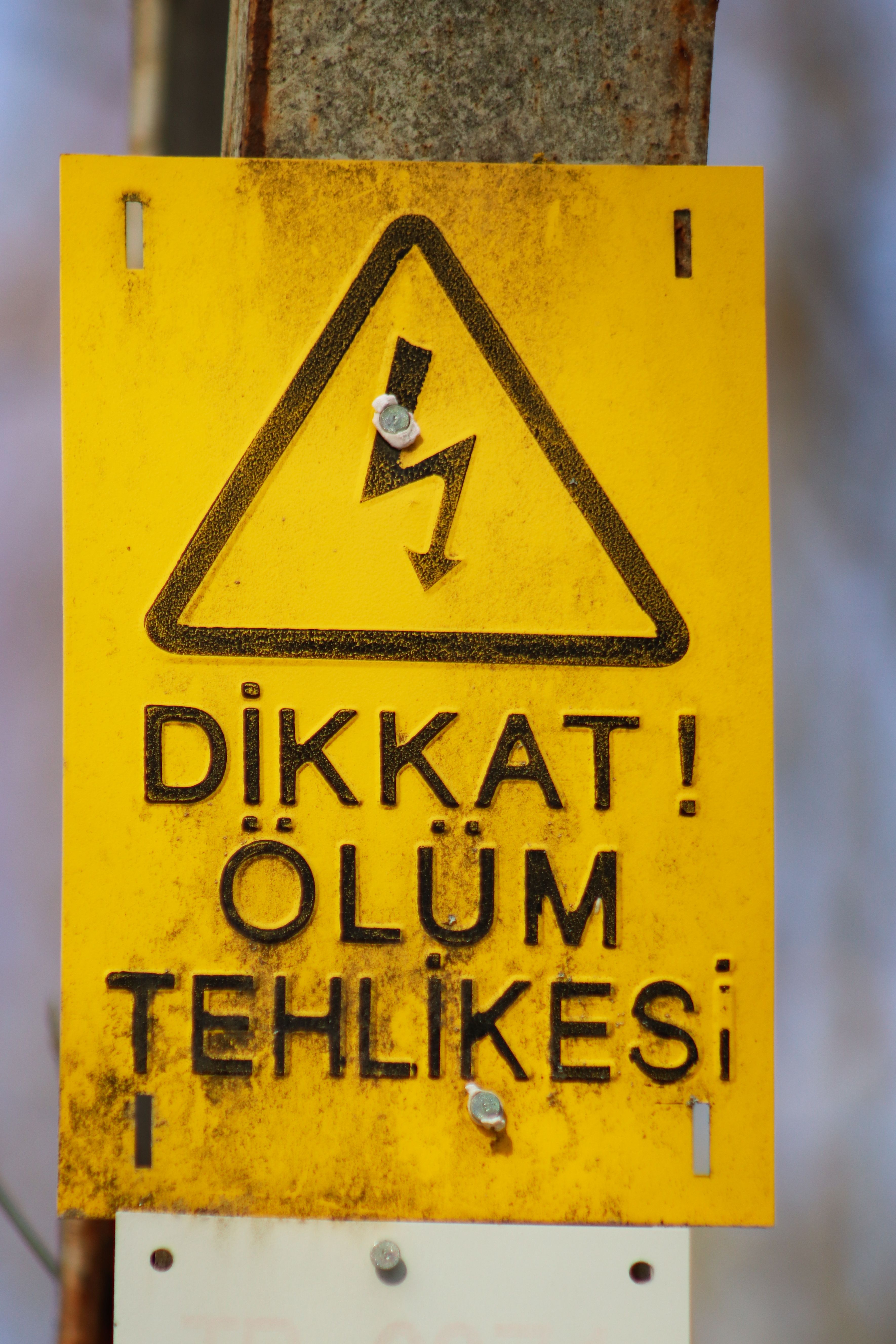 Bright yellow warning sign indicating danger in Turkish with symbols.