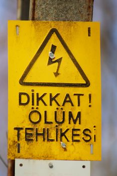 Bright yellow warning sign indicating danger in Turkish with symbols.