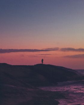 一位独身的渔夫在海浪映衬下，映出充满活力的日落
