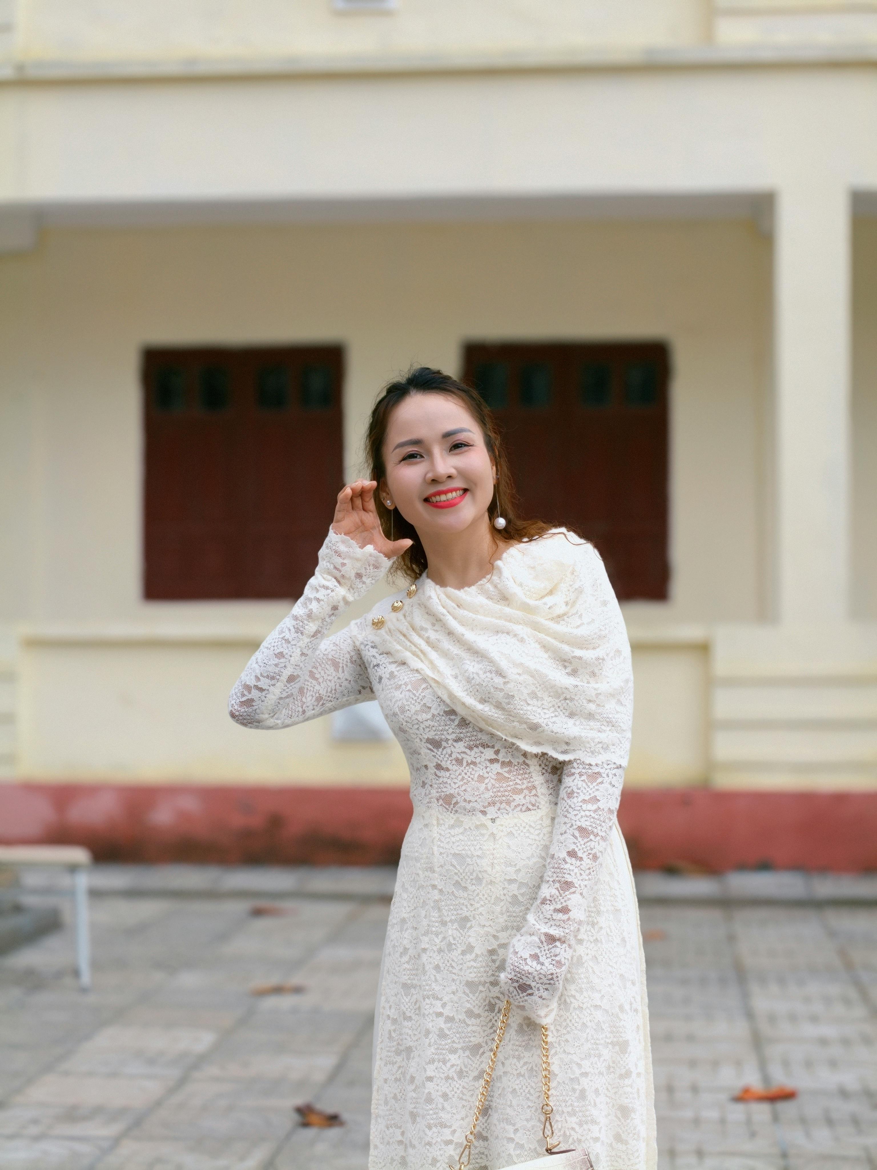 無料 白いレースのドレスを着て屋外で微笑み、優雅さと落ち着きを醸し出す魅力的な女性。 写真素材