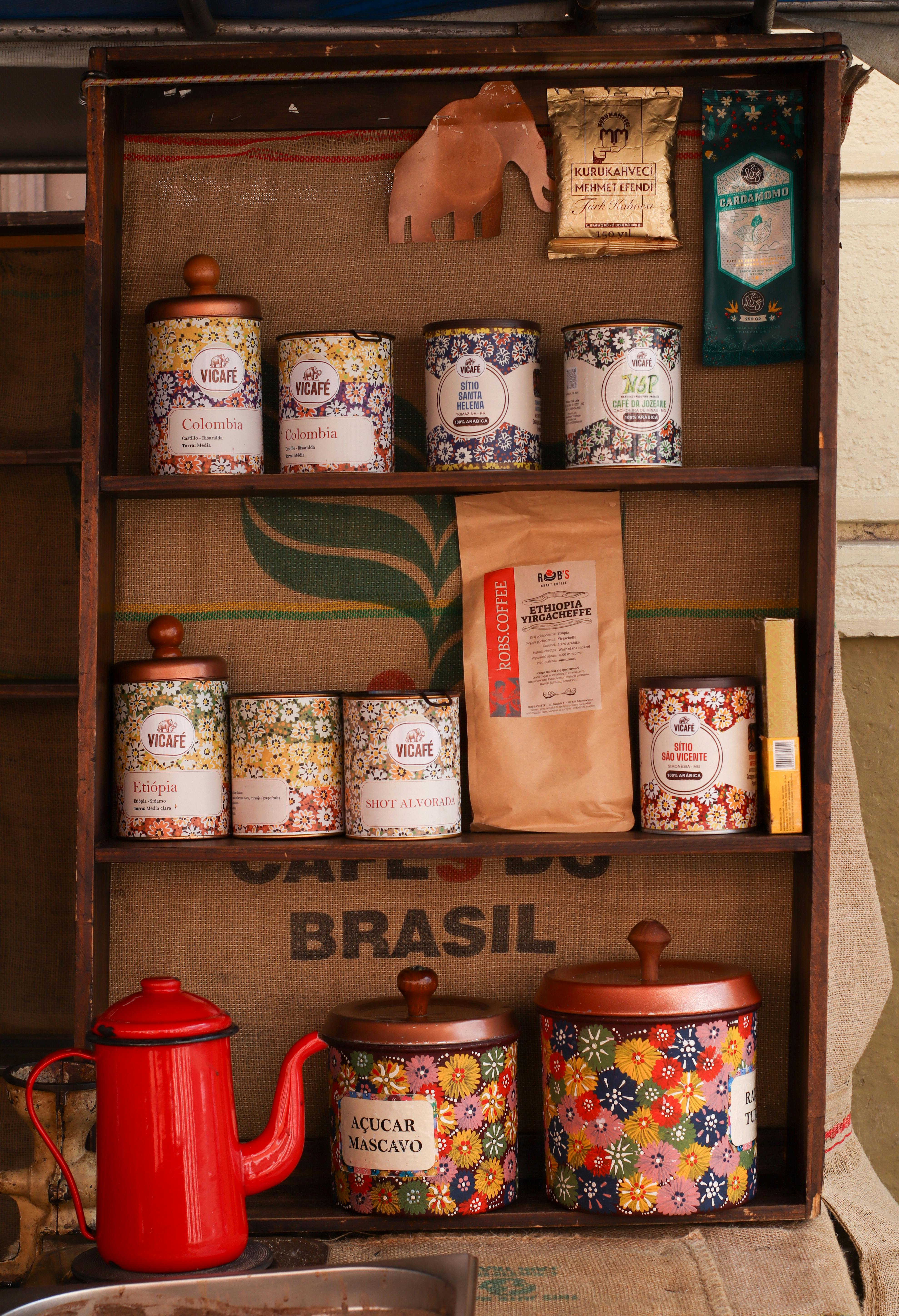 бесплатная На полке стоят красочные винтажные жестяные коробки для хранения кофе и чая, а рядом — красный чайник. Стоковое фото