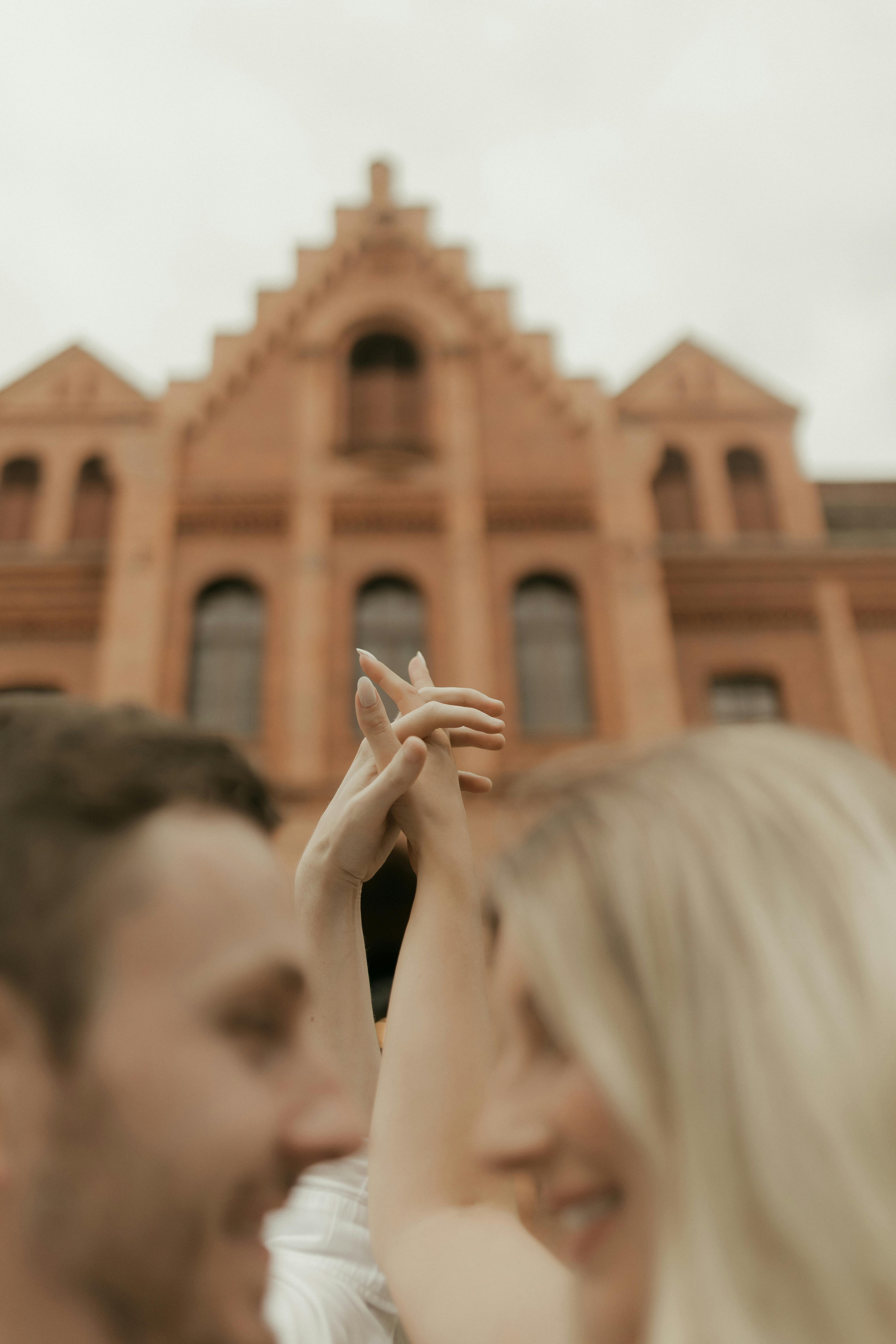 無料 歴史的なレンガ造りの建物の前で手をつないでいるぼやけたカップルが、愛情と親密さを伝えています。 写真素材