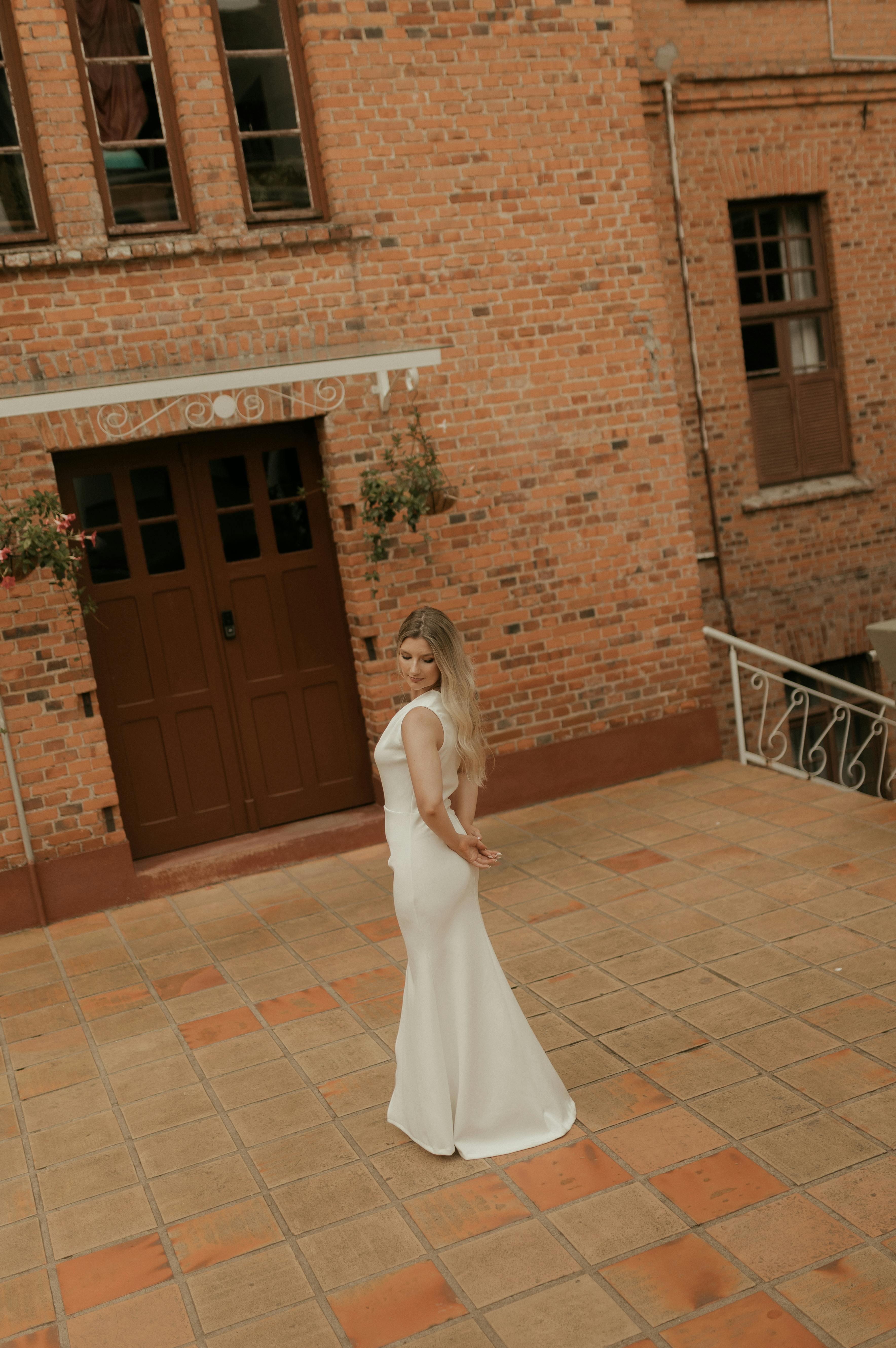 бесплатная Прекрасная невеста в белом платье грациозно стоит перед старинным кирпичным зданием. Стоковое фото