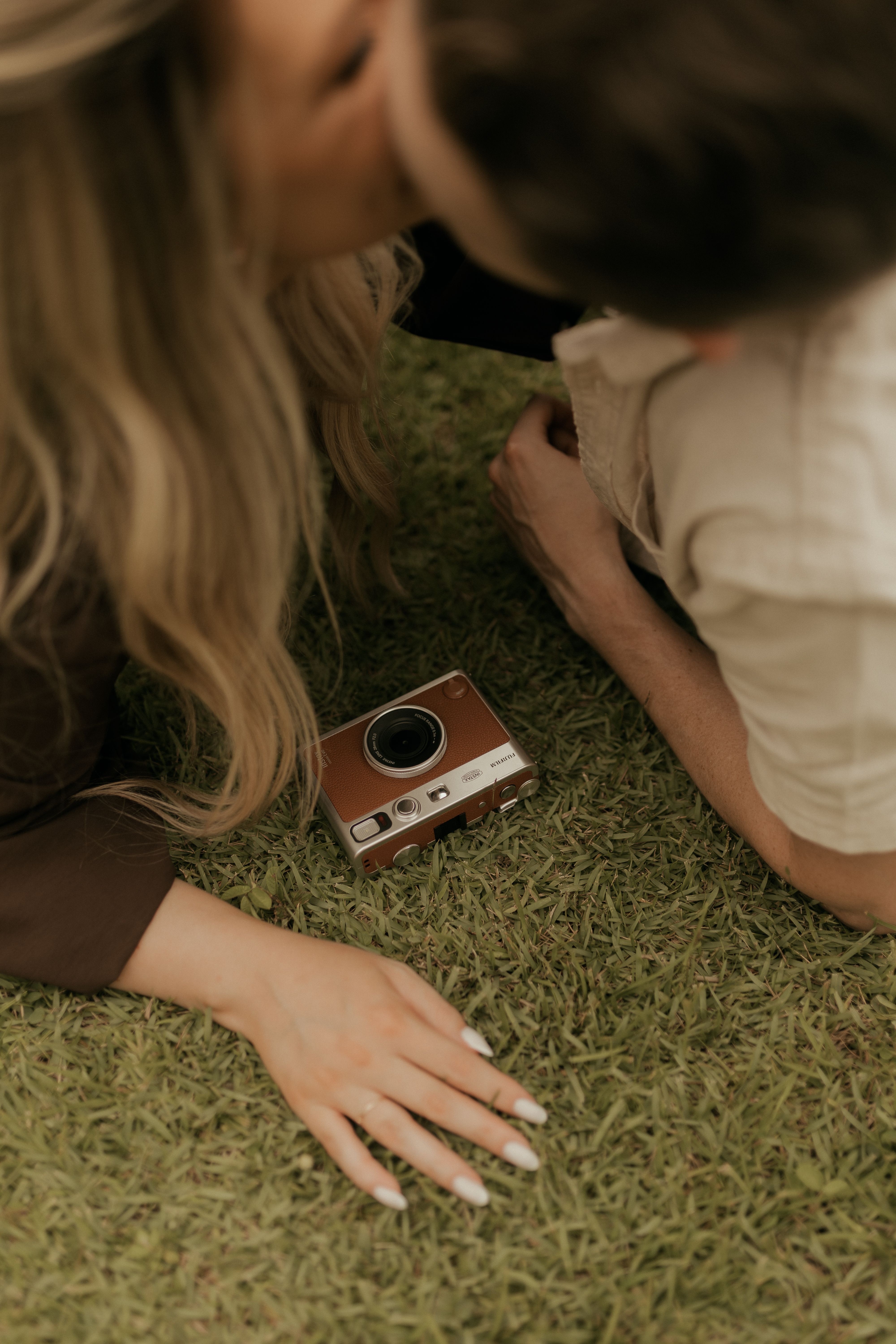 A couple enjoying a romantic moment outdoors on grass with a classic camera in view.