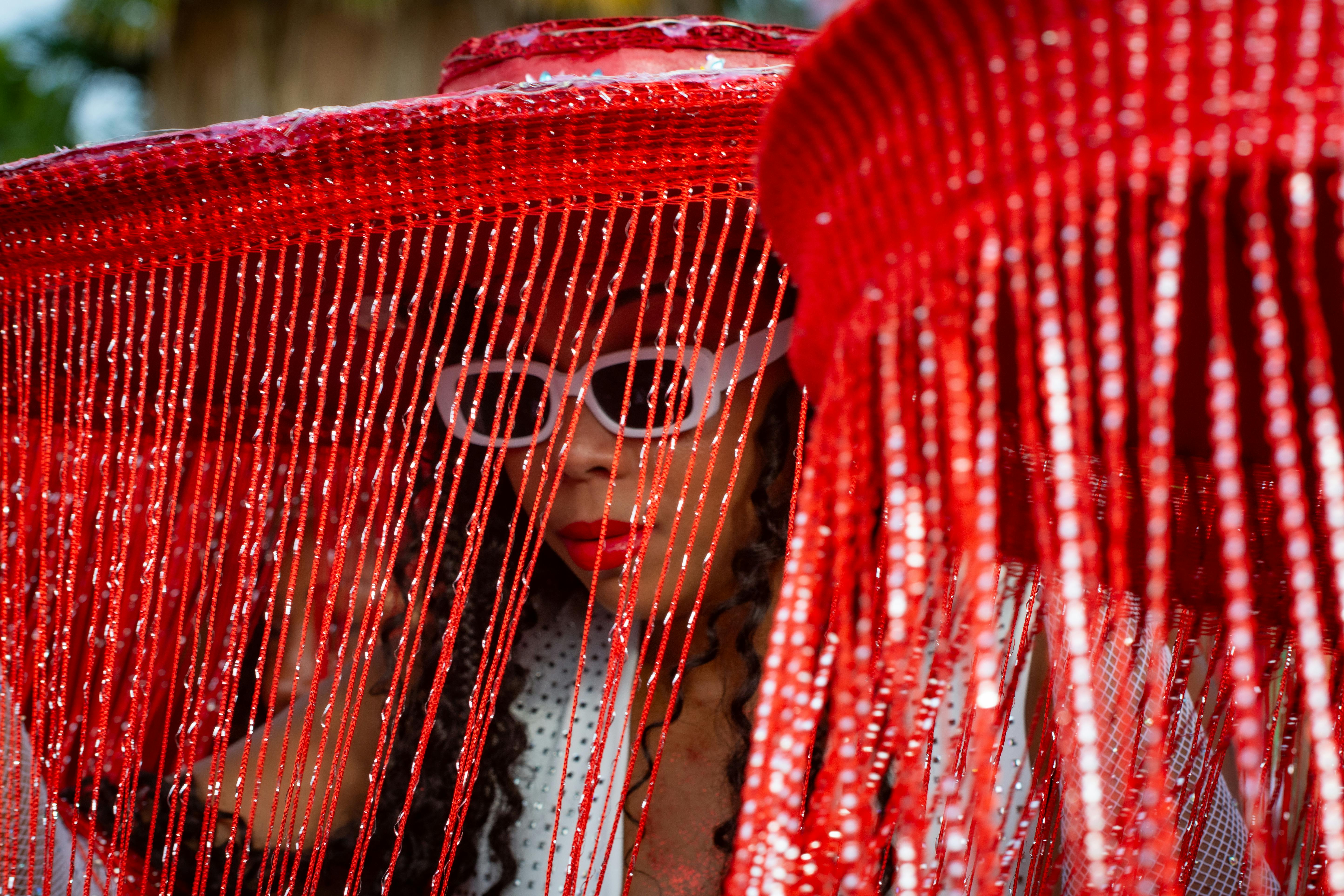 Free Vibrant portrait featuring a person behind a red fringe hat outdoors. Stock Photo