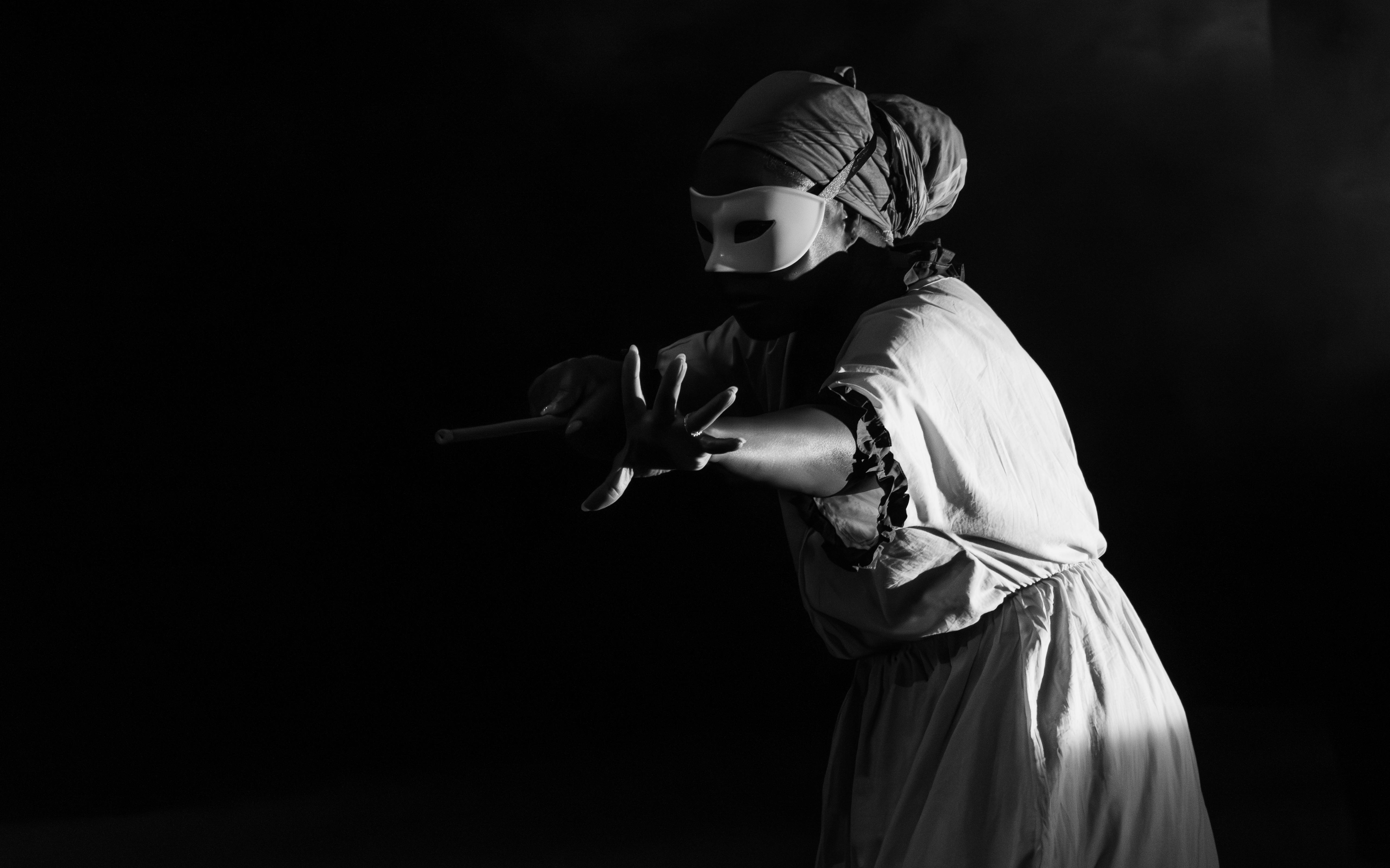 Gratis Svart-hvitt-bilde av en maskert utøver i teaterkostyme som strekker seg dramatisk under et sceneopptreden. Arkivbilde