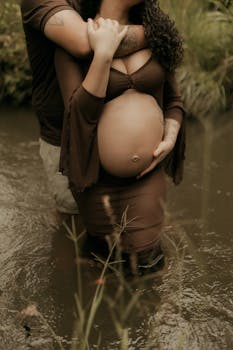 Pregnant woman embraced by partner in peaceful creek setting, showcasing love and anticipation.