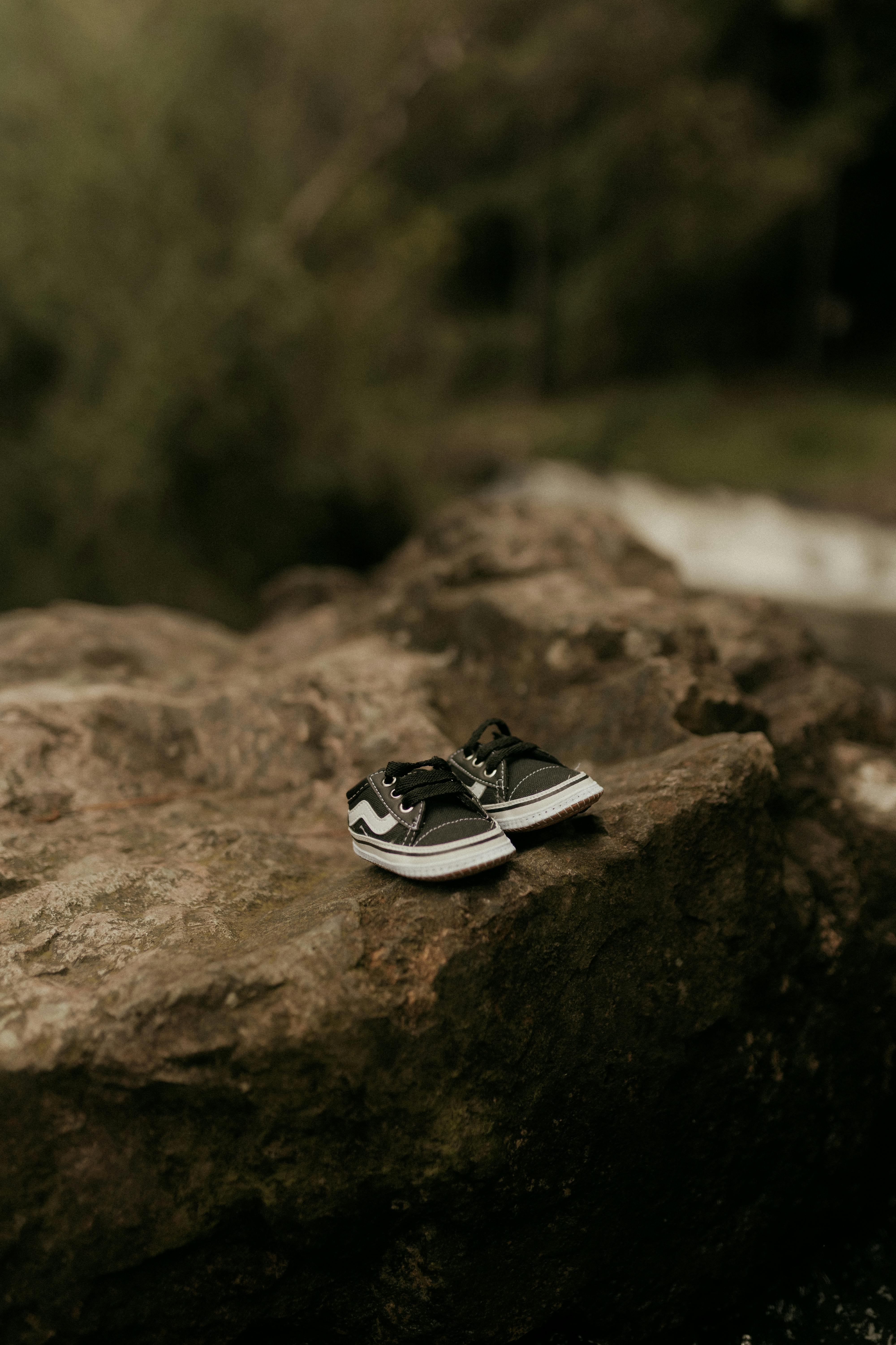 gratis Zwarte sneakers staan ​​op een kunstzinnige manier op een rotsachtige ondergrond in een buitenomgeving. Stockfoto