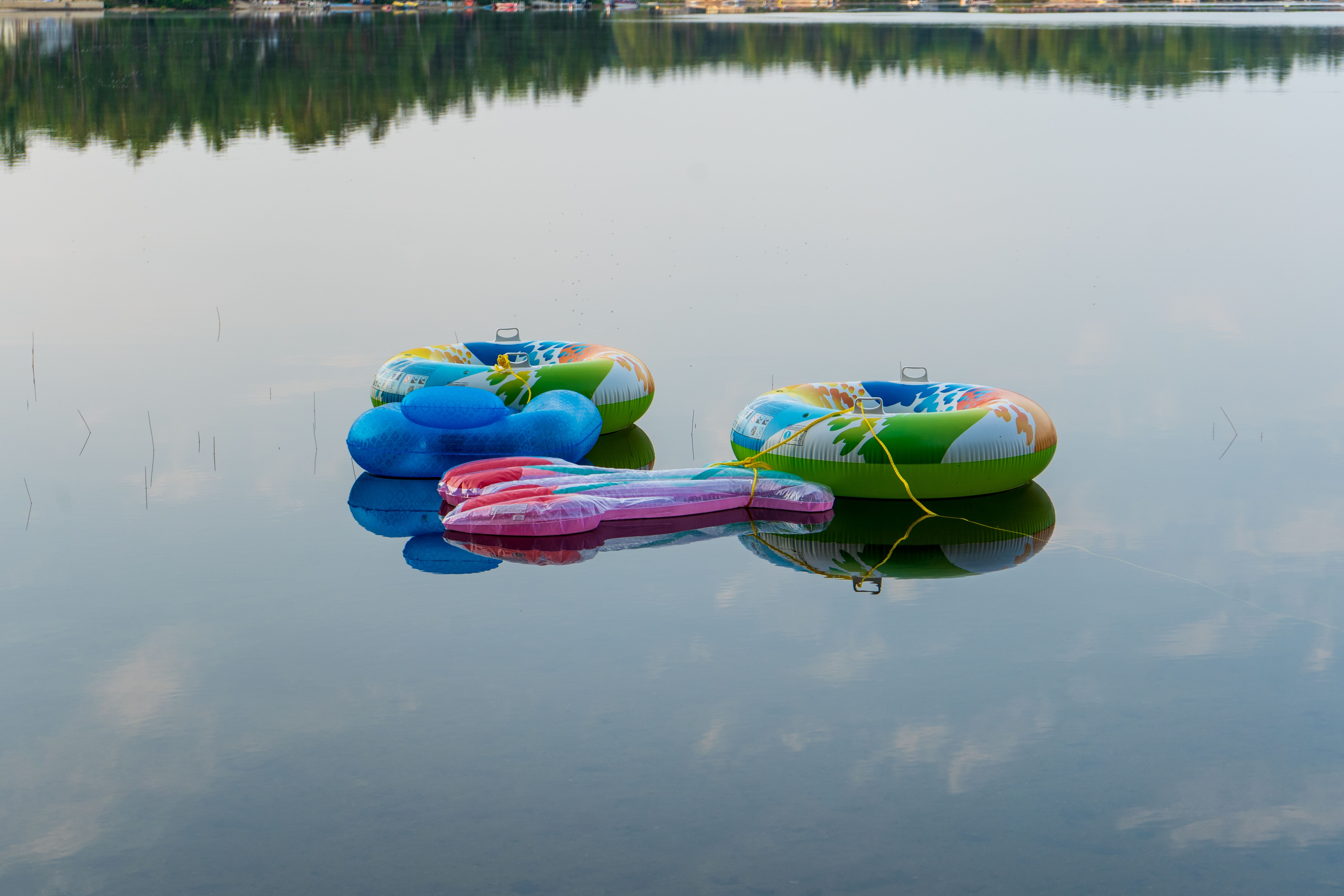 Three vibrant inflatable tubes resting on a serene lake, reflecting the peaceful water surface.