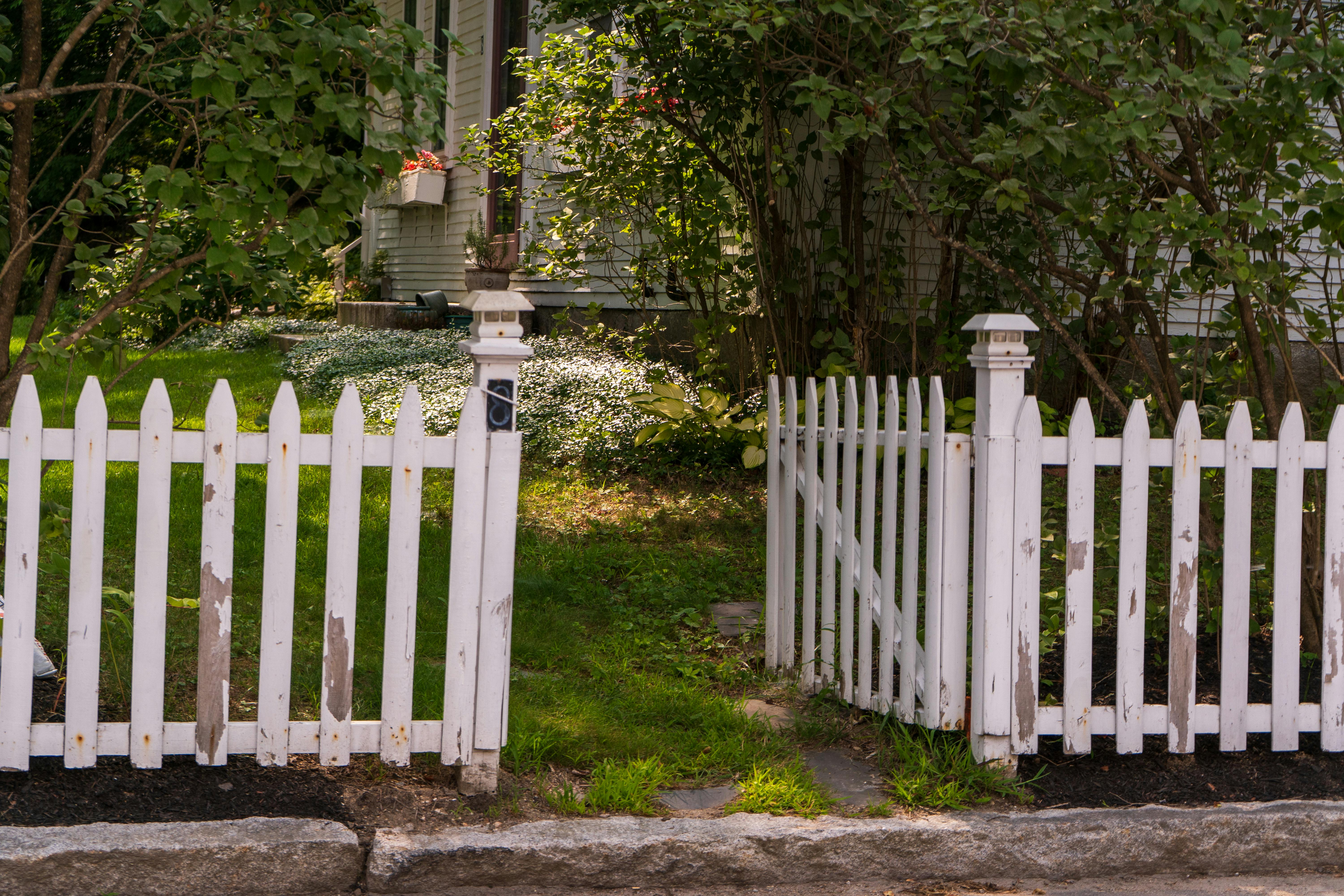 無料 伝統的な家屋の横にある緑豊かな庭園に白いピケットフェンスがあります。 写真素材