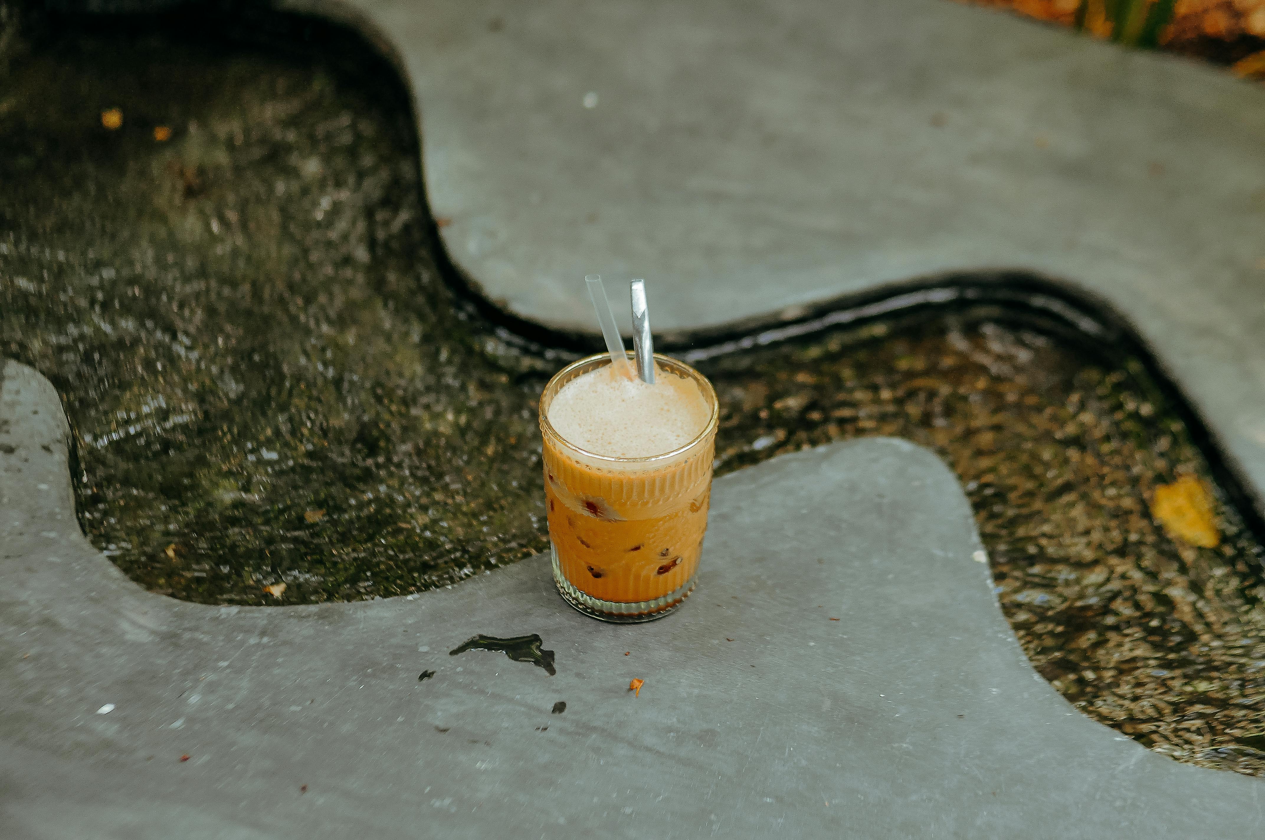 Free A glass of iced coffee with two straws sits on a stone surface next to a flowing stream. Stock Photo