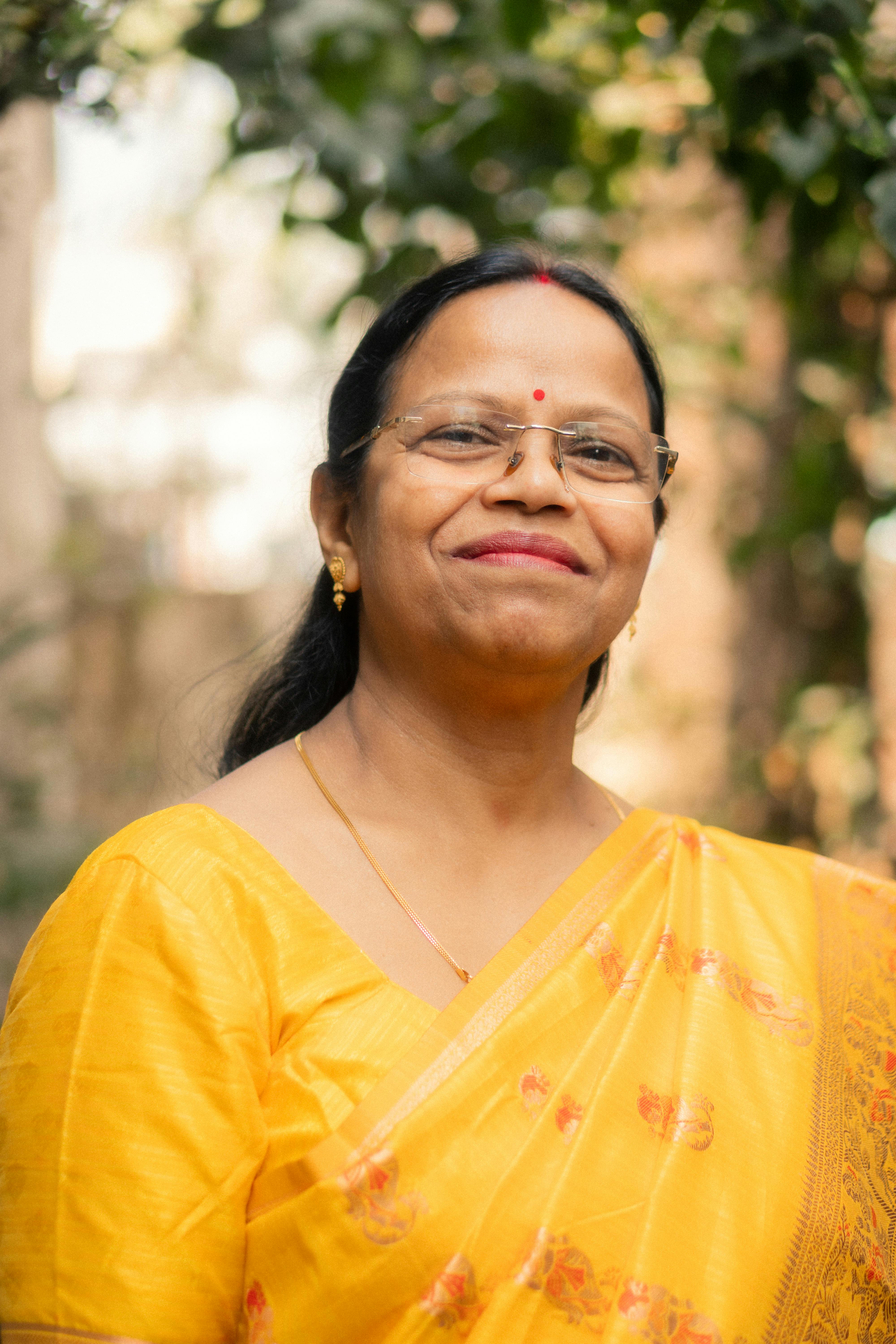 Serene outdoor portrait of a smiling woman in a vibrant yellow saree with lush green background.
