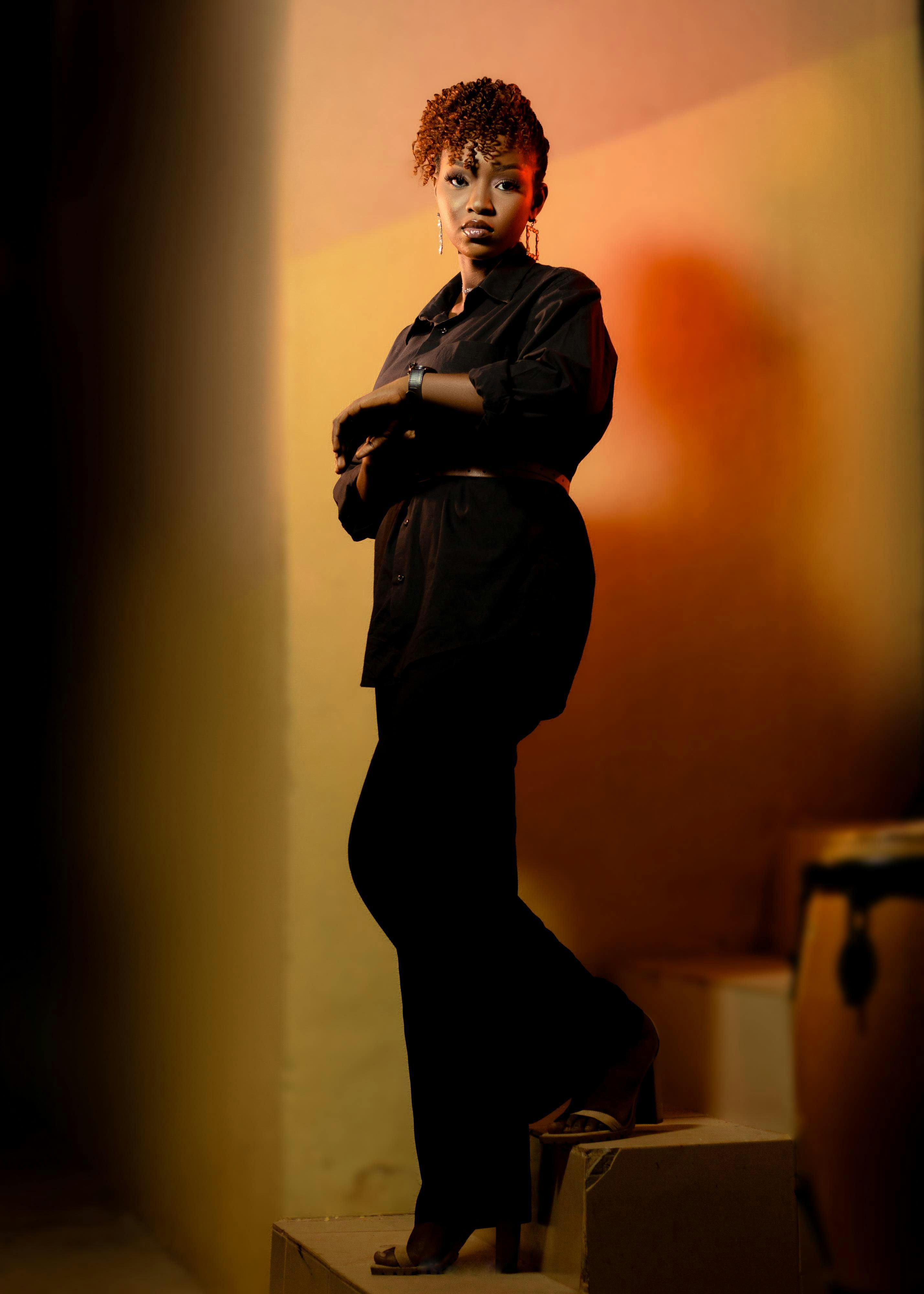 Gratis Elegant portrett av en kvinne i et svart antrekk med varmt lys og en stemningsfull bakgrunn. Arkivbilde