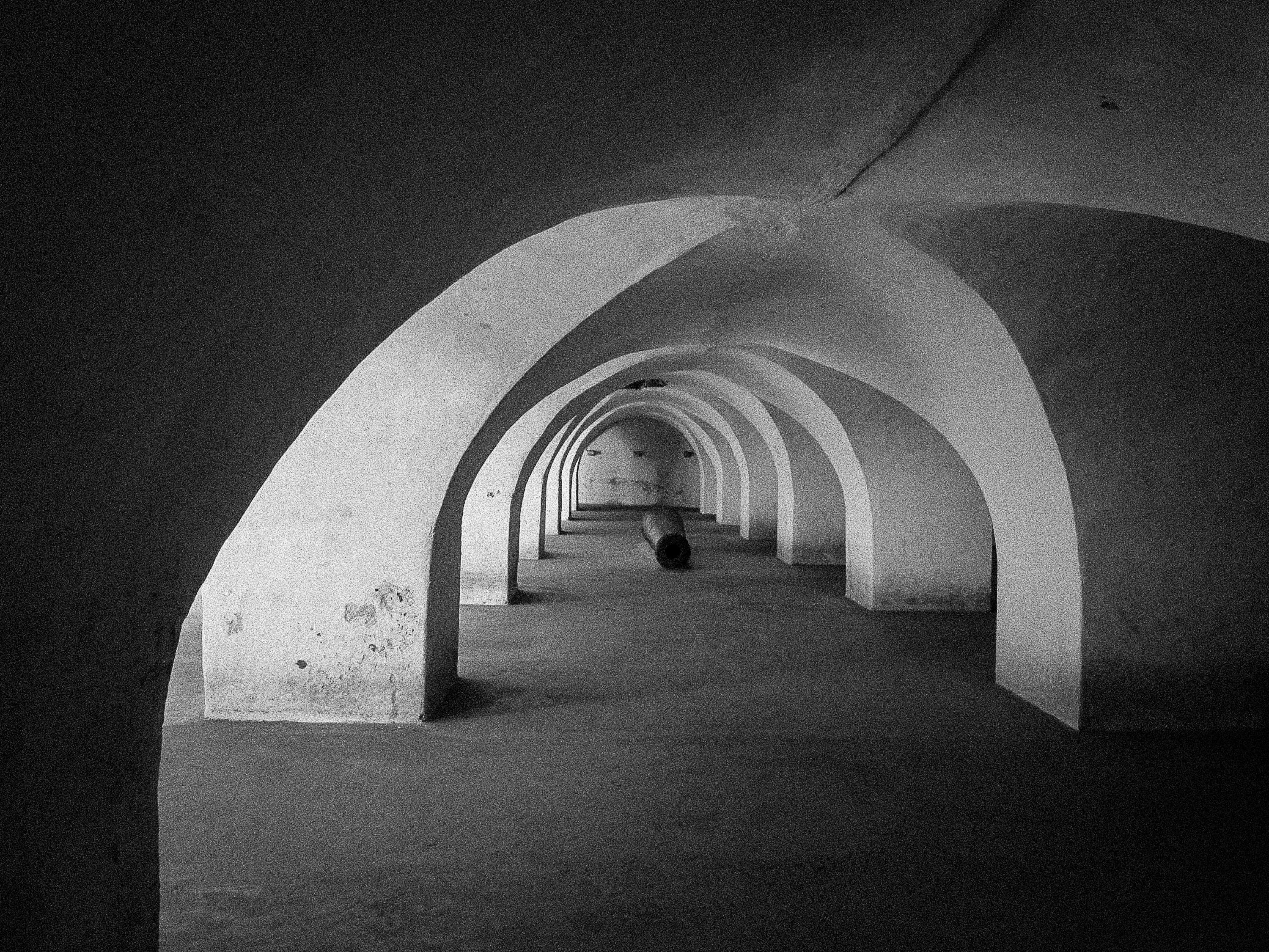 Gratis Foto hitam putih sebuah koridor lengkung kuno, menciptakan perspektif terowongan yang dramatis. Foto Stok