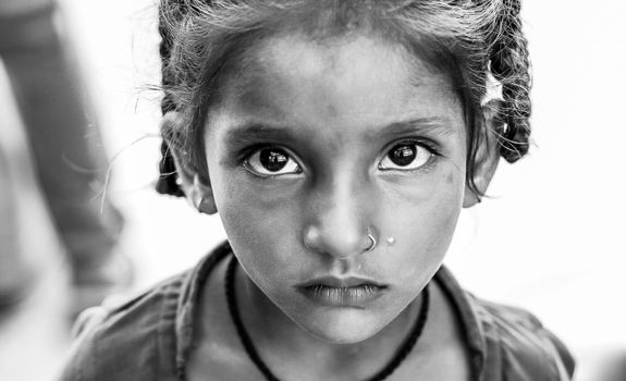 A striking black and white portrait of a young girl staring directly into the camera with deep, expressive eyes.