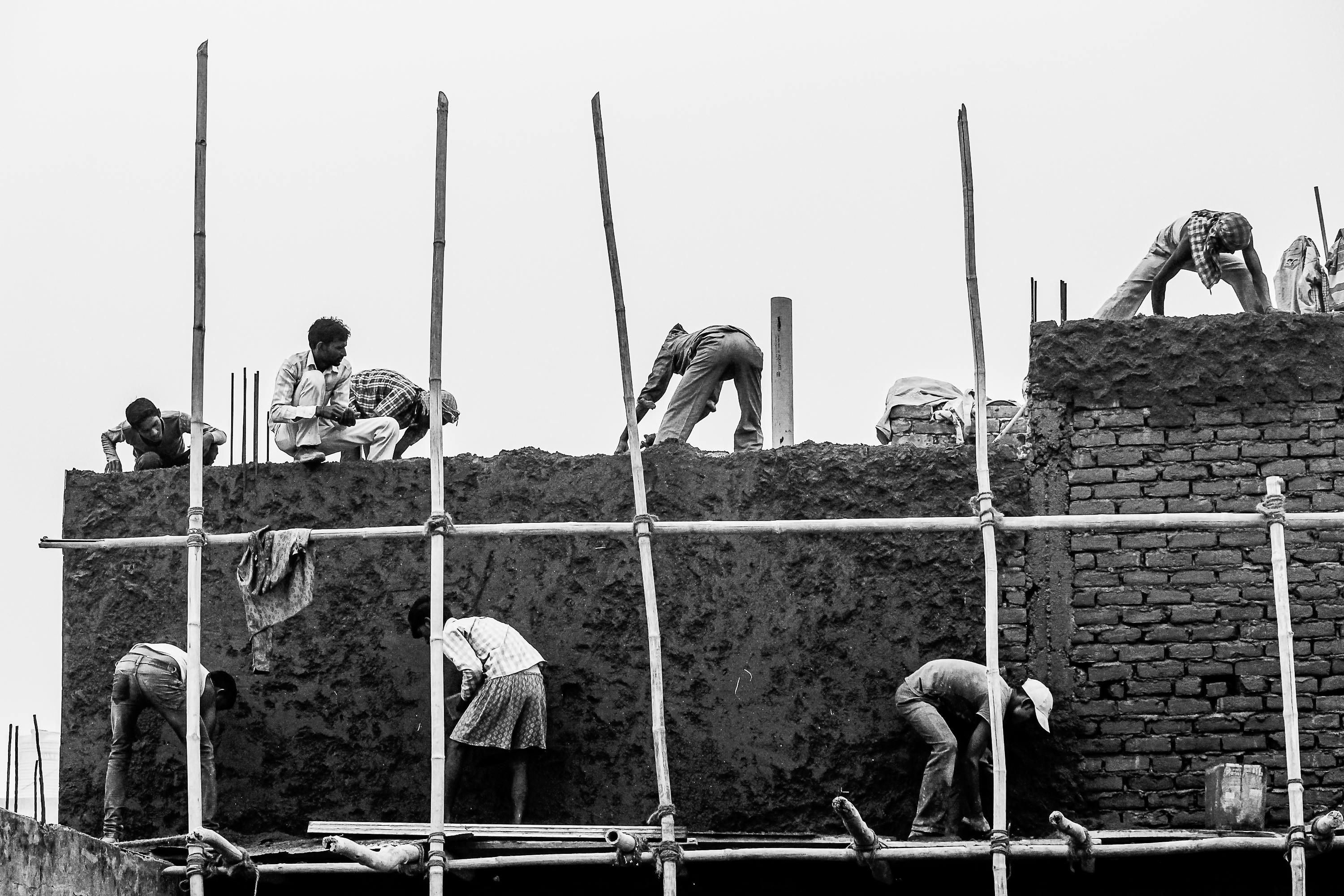 бесплатная Рабочие-бетонщики на строительных лесах возводят кирпичную стену — снимок в черно-белом цвете. Стоковое фото