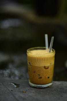A refreshing iced coffee served in a vintage glass with straws, set against an outdoor background.
