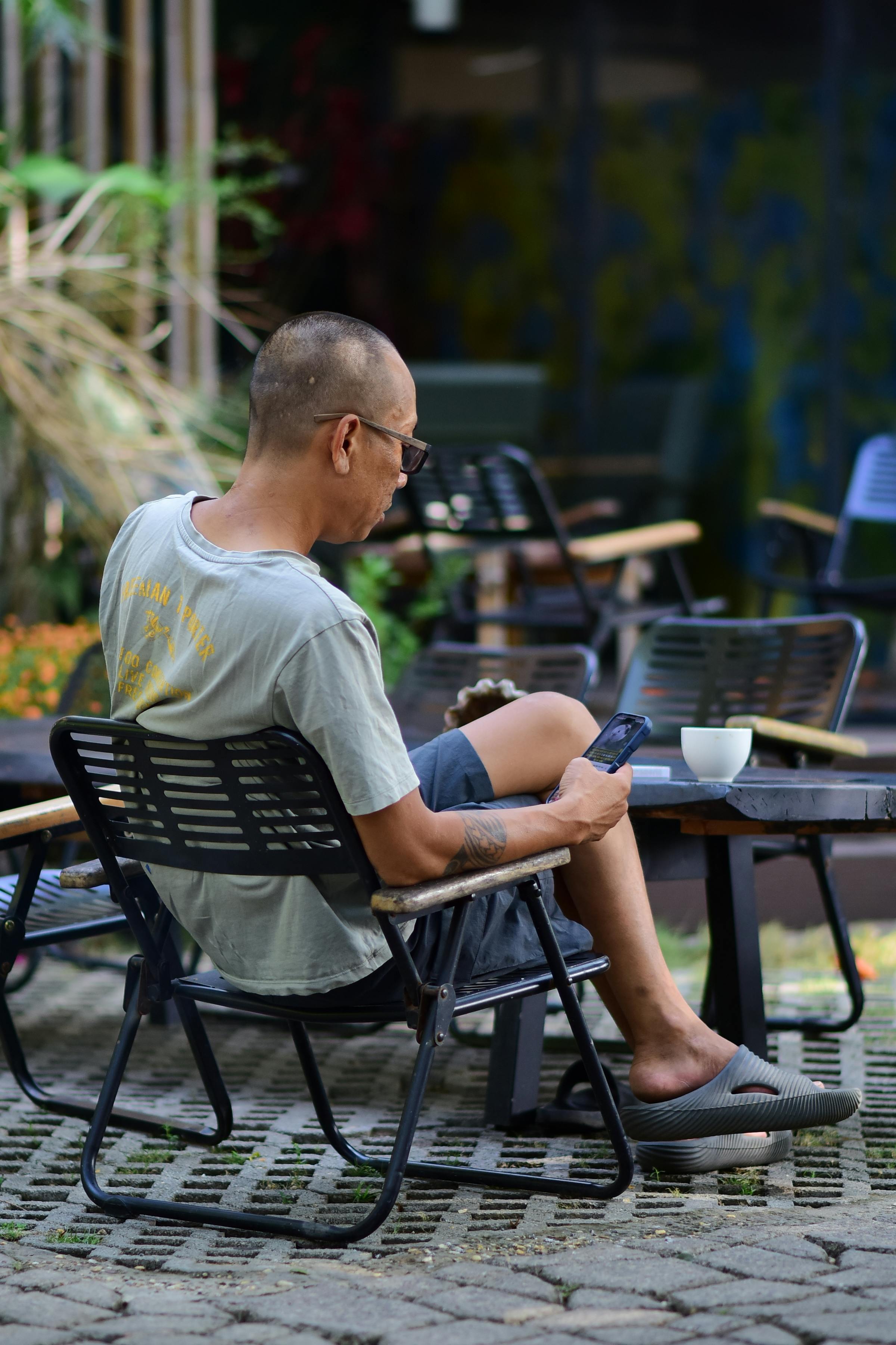 Free Casual outdoor cafe setting with man seated and using smartphone. Stock Photo