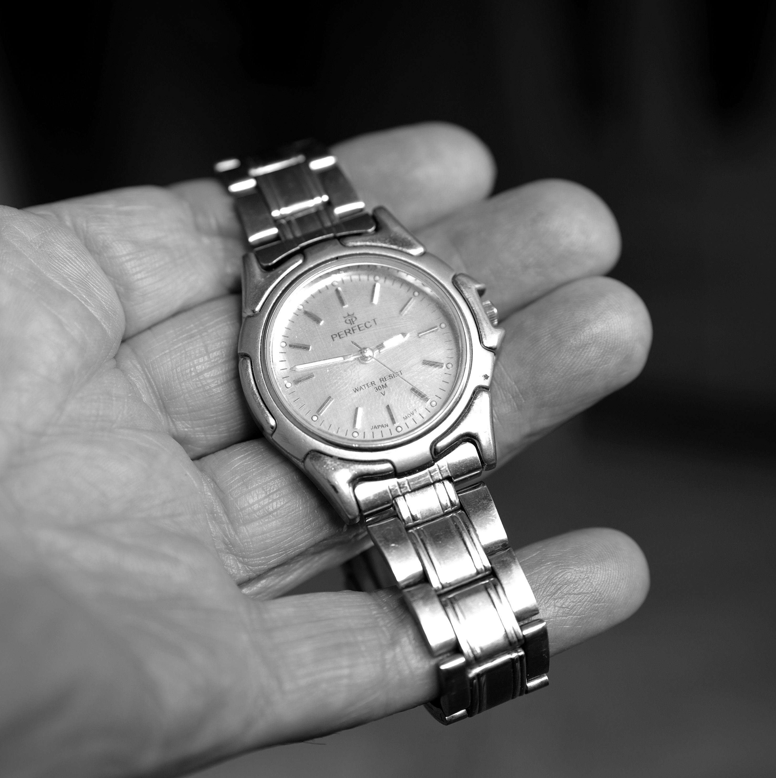 Grayscale photo of a silver wristwatch held in an open hand, showcasing elegant design.