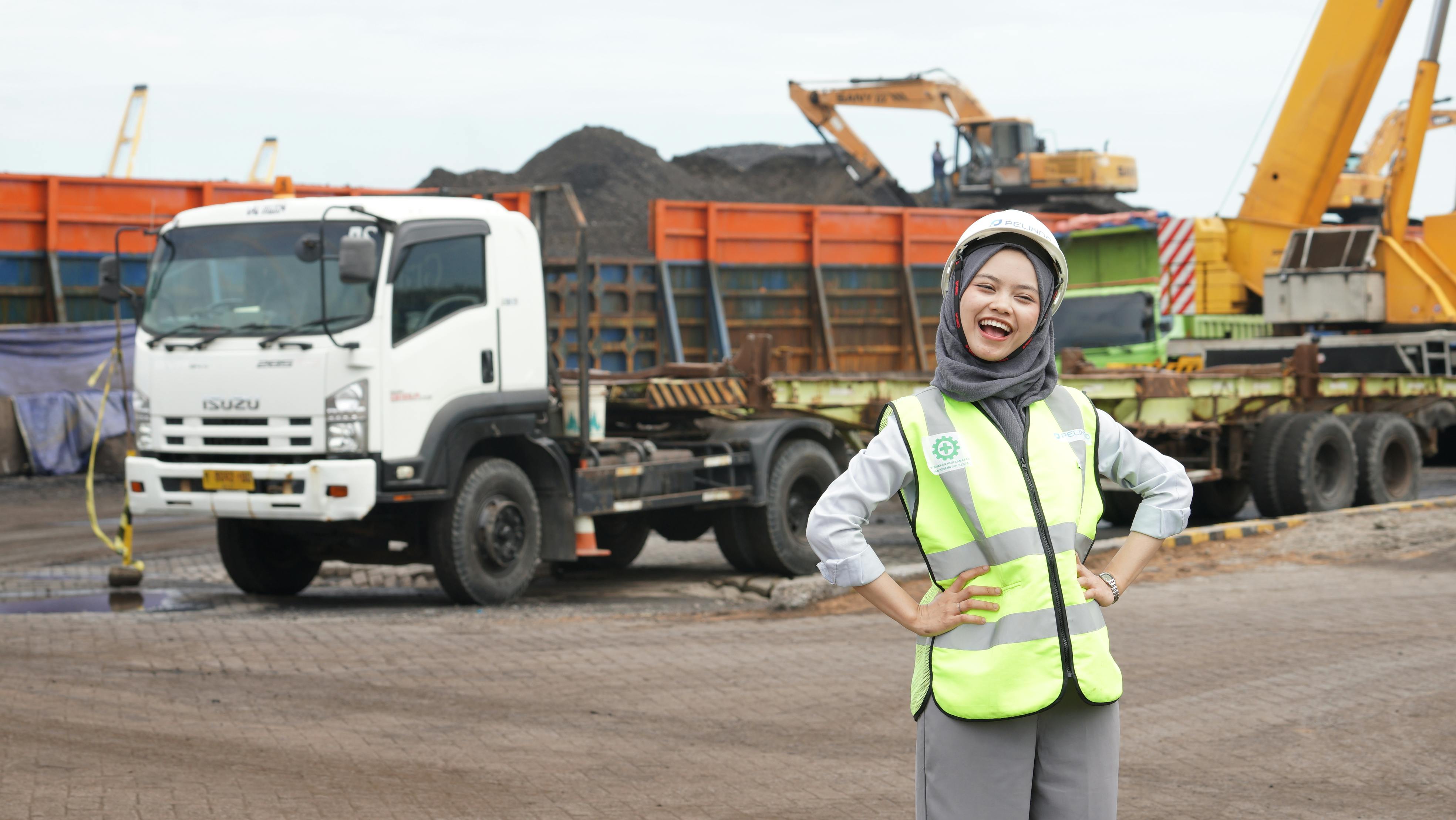Female worker with safety gear at a bustling construction site with trucks and excavators.