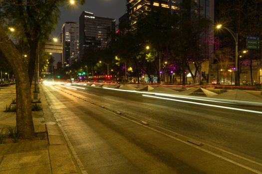 Vibrant nighttime view of a busy boulevard in Mexico City, showcasing light trails and skyscrapers.