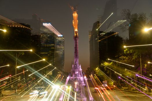 Long exposure capturing light trails around Angel of Independence monument at night in Mexico City.