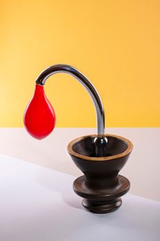 A modern sculpture featuring a red drop and black base against a vibrant yellow background.