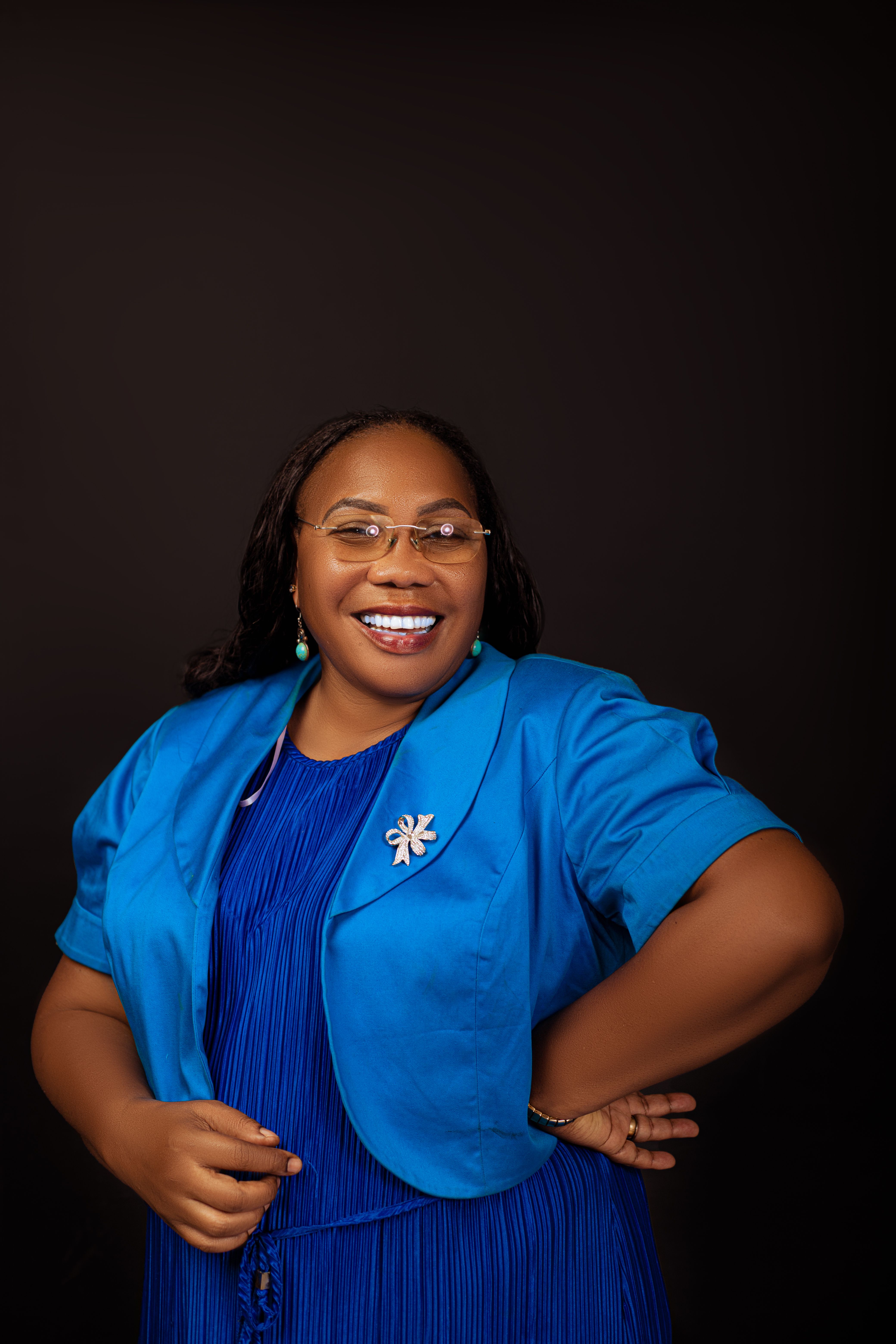 Portrait of a smiling woman in a vibrant blue outfit on a dark background.