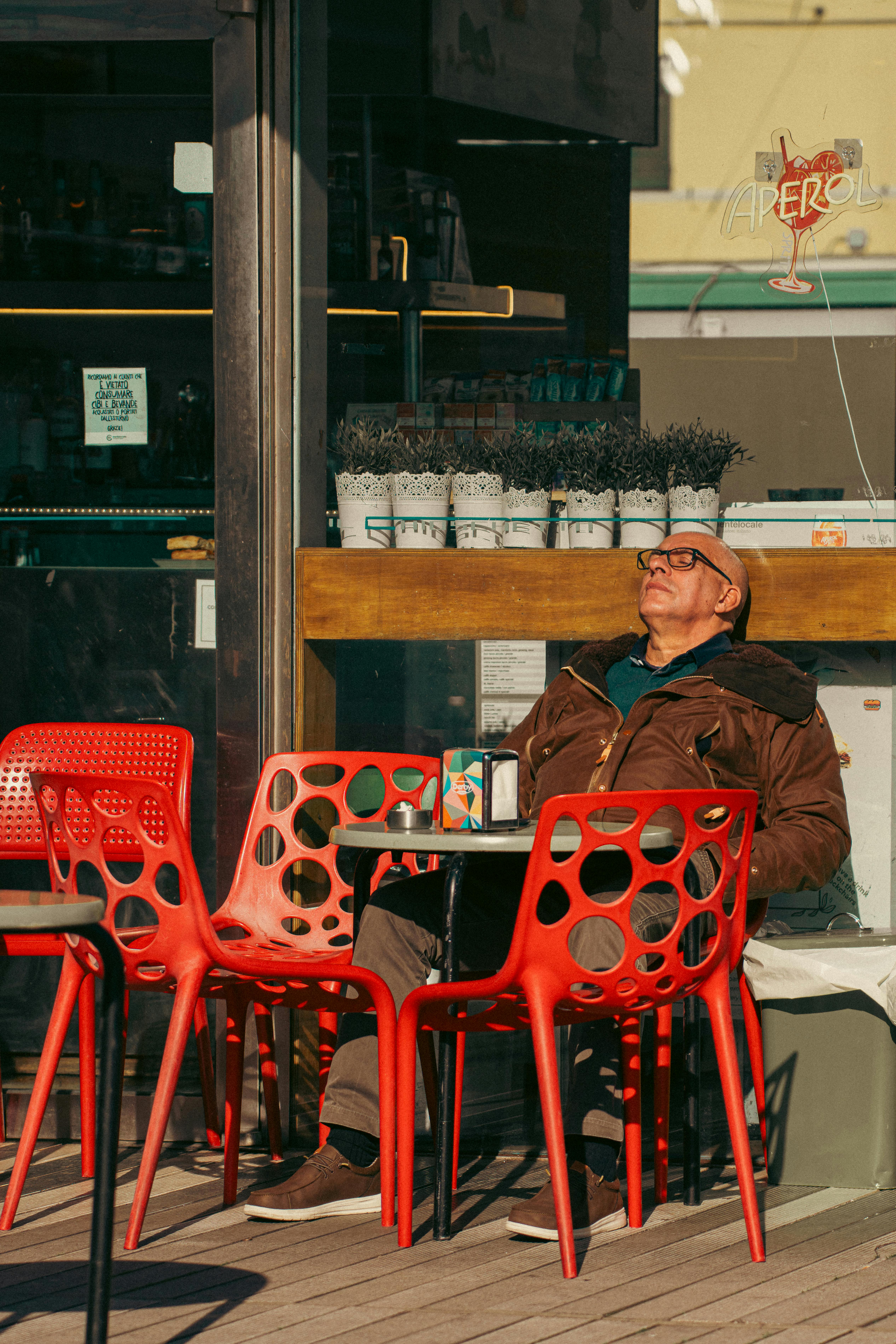бесплатная Пожилой мужчина наслаждается солнечным днем ​​в уличном кафе в Генуе, Италия. Яркие красные стулья добавляют красок. Стоковое фото